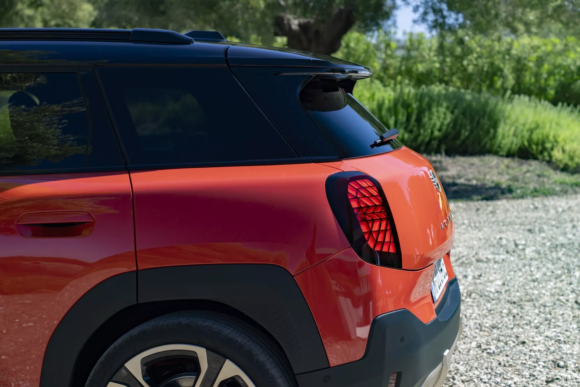 Close-up view of the 2024 MINI Aceman (J05) rear section with LED taillight, metallic red paint, and alloy wheel, in a natural outdoor setting