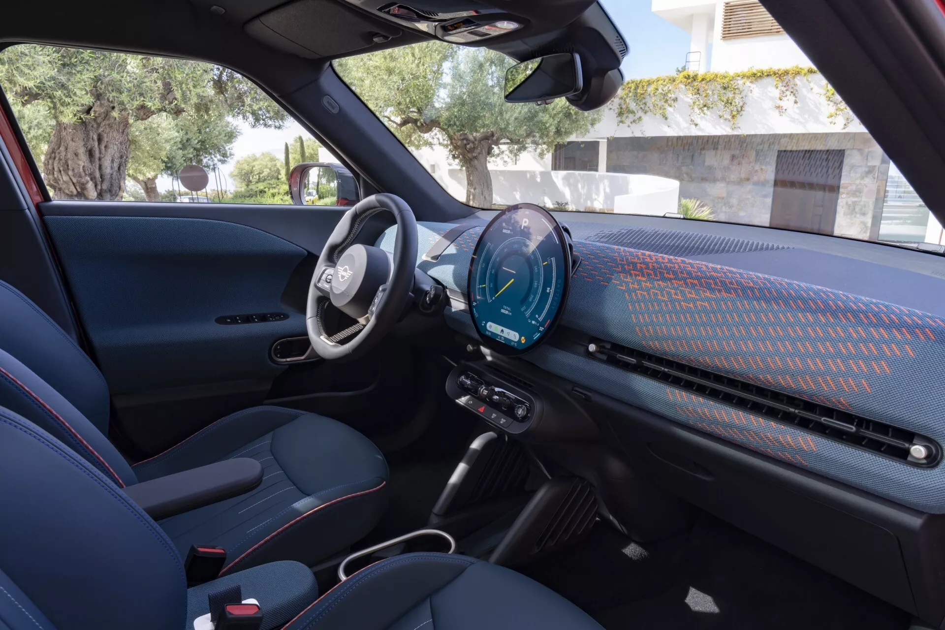 Interior view of the 2024 Mini Aceman (JO5) from the passenger side, showcasing its digital cockpit, central infotainment touchscreen with connectivity features, minimalist control panel, sporty two-tone seats with red accent stitching, and advanced technology and safety features.