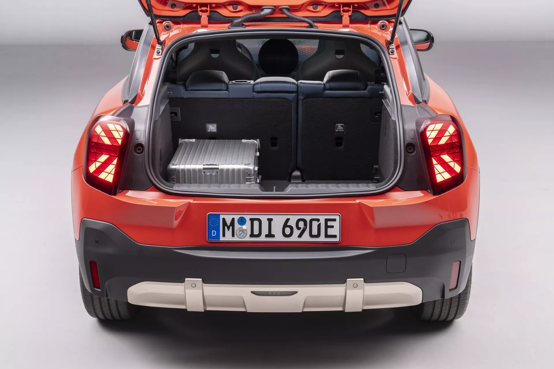 Rear view of a 2024 Mini Aceman (J05) hatchback with open tailgate, revealing the spacious trunk space and showcasing rear design features including tail lights, bumper with parking sensors, and badging indicative of electric or hybrid technology, photographed from an elevated angle.