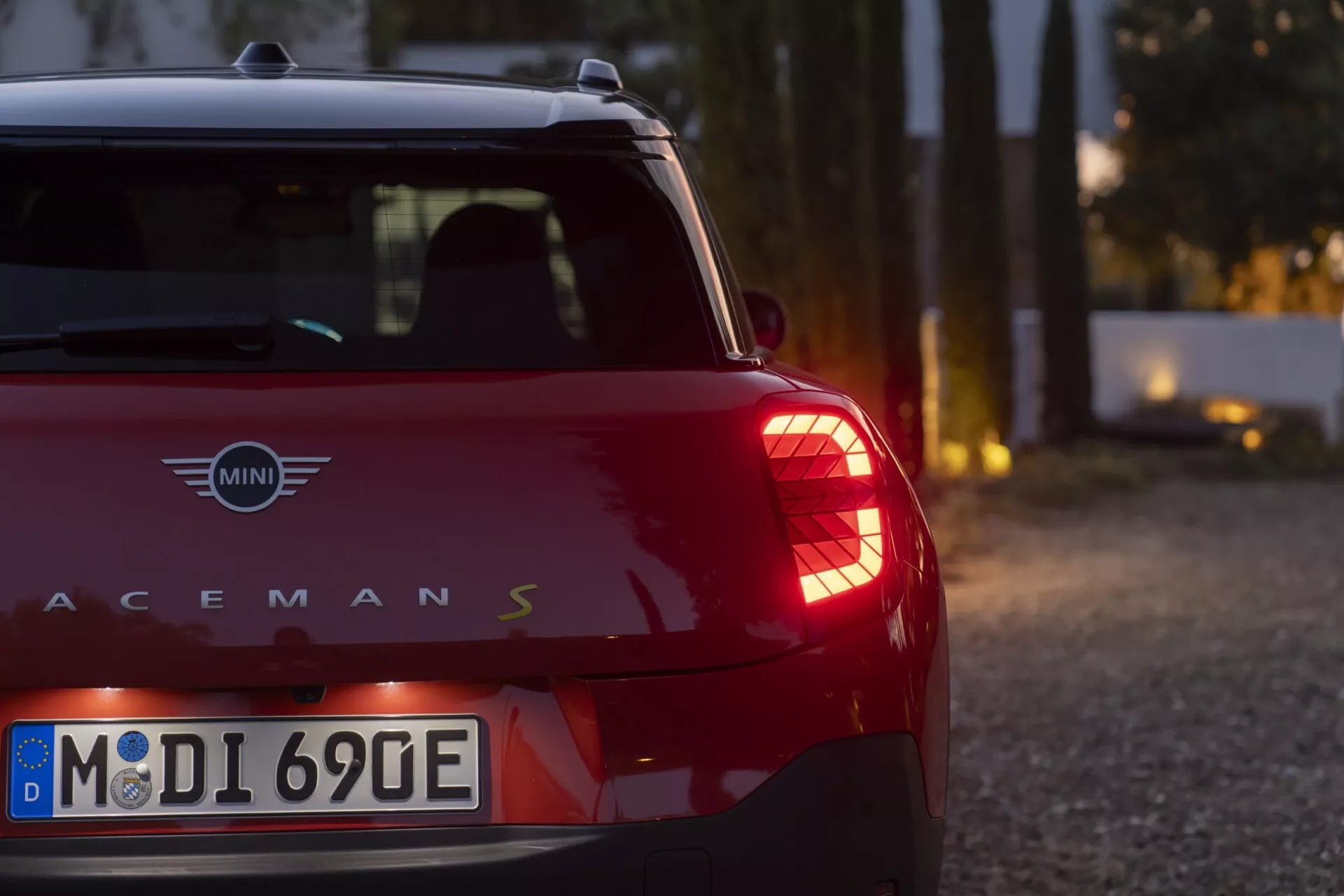 Close-up view of the rear side of a red MINI Paceman S model 2024 (J05) under soft lighting, highlighting distinctive vertical rear lights and metallic logo detailing.