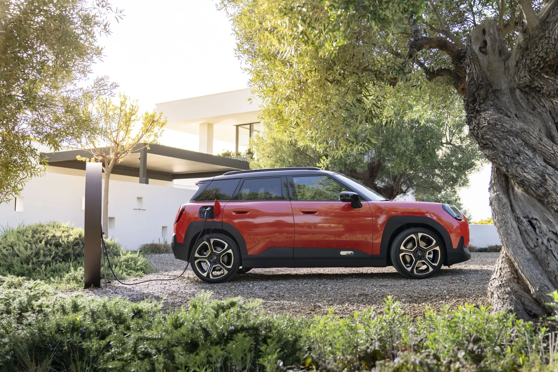 2024 Mini Aceman (J05) showcased in a luxurious setting, featuring a modern SUV design with a two-tone body, contrasting black roof, tinted windows, and sporty alloy wheels, parked on a gravel driveway with residential greenery and a possible EV charging station indicating advanced technology and eco-friendliness