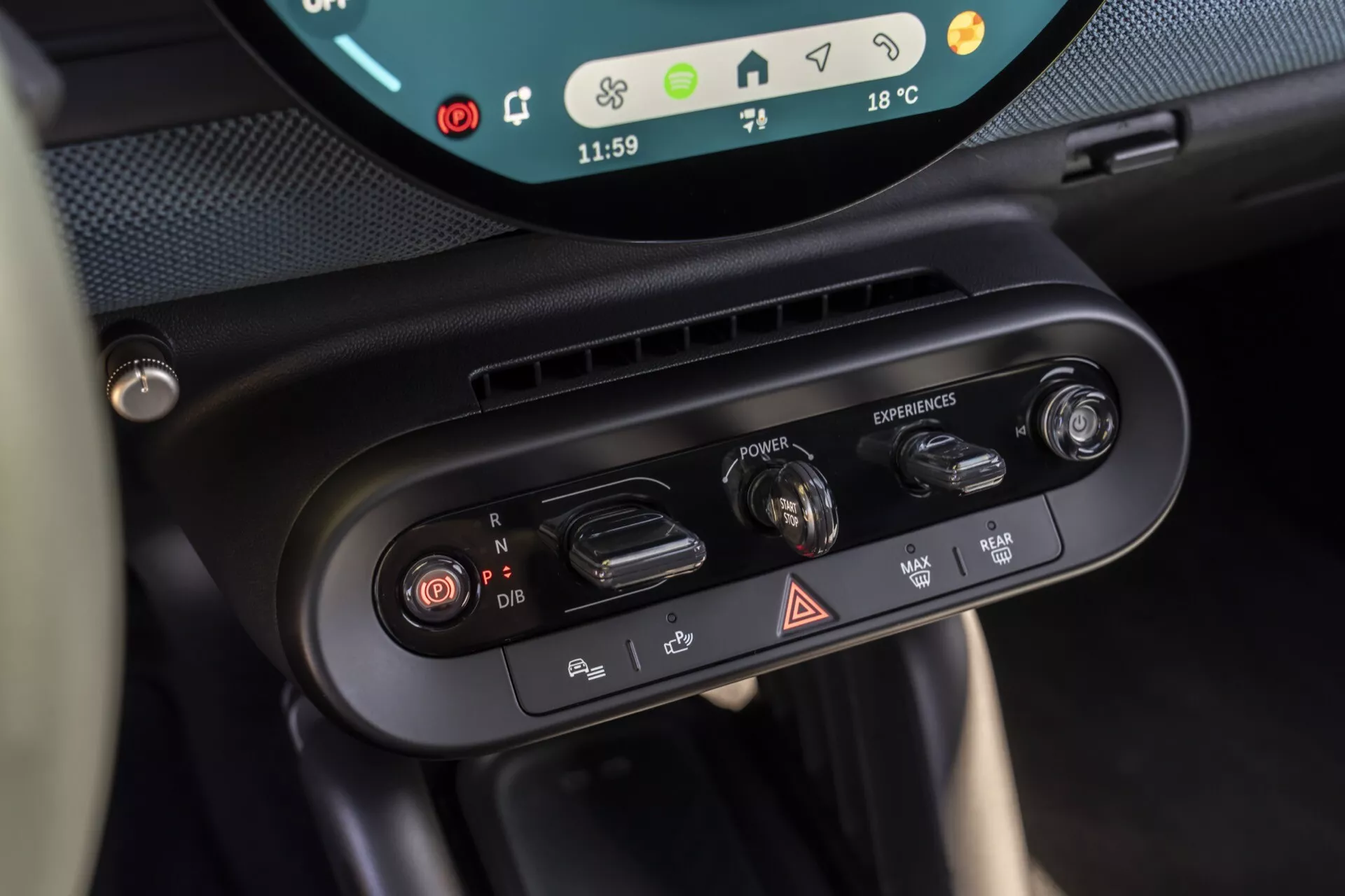 Close-up view of the 2024 Mini Aceman (JO5) climate control dials and driving mode selector, showcasing dual-zone climate settings, air circulation buttons, hazard light switch, and driving mode rotary dial with a glimpse of the digital display indicating time and exterior temperature