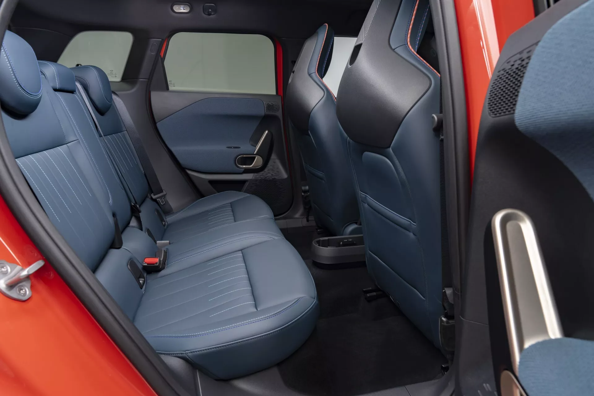Interior view of the 2024 Mini Aceman (J05) focusing on the rear passenger compartment, showcasing the patterned textile upholstery and seat design for enhanced comfort, with a visible door featuring power window controls and speaker grilles.