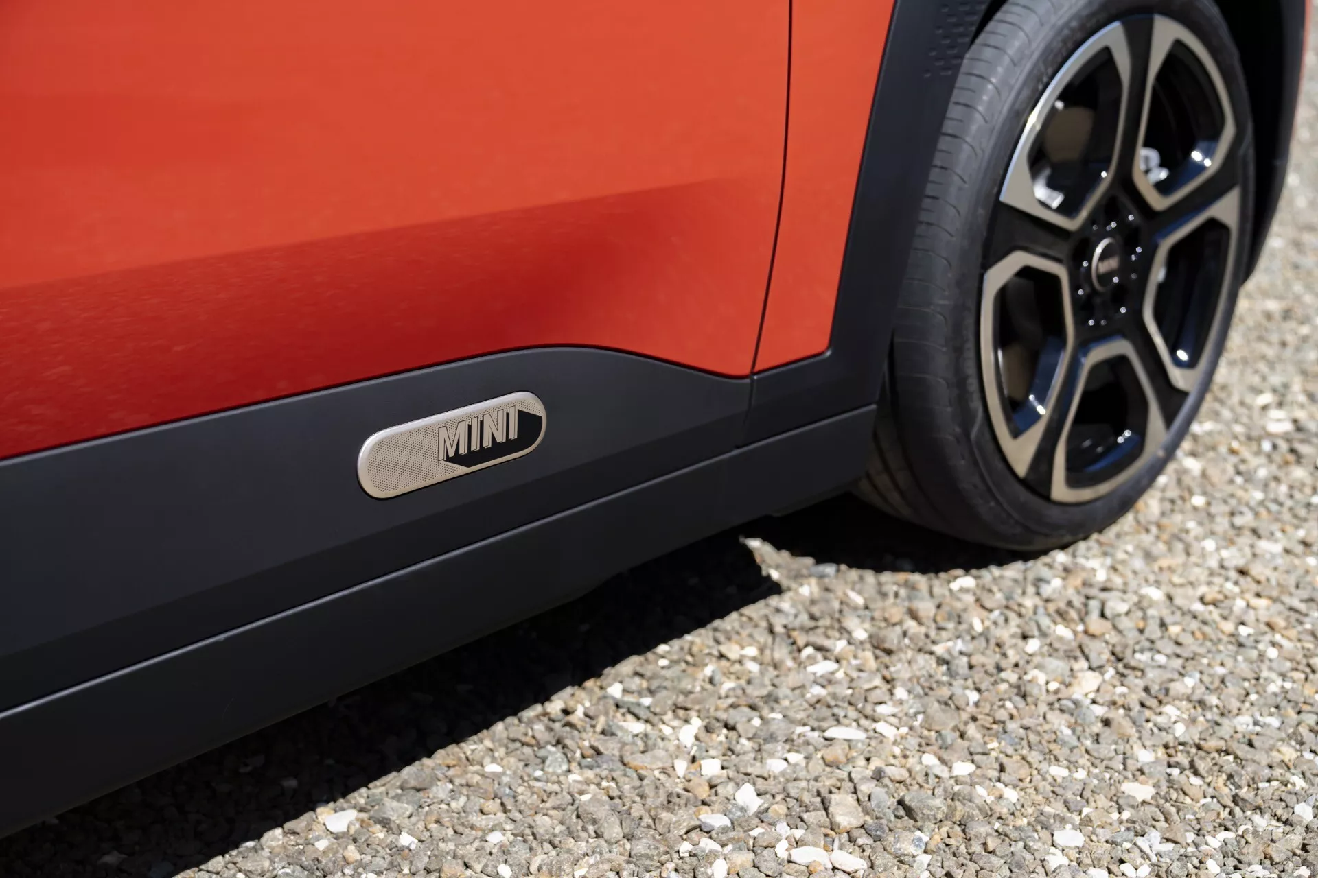 Close-up of the Mini Aceman 2024 (J05) showcasing the car's lower side, rear wheel with multi-spoke design, vibrant red body color, and distinctive side skirt with MINI emblem