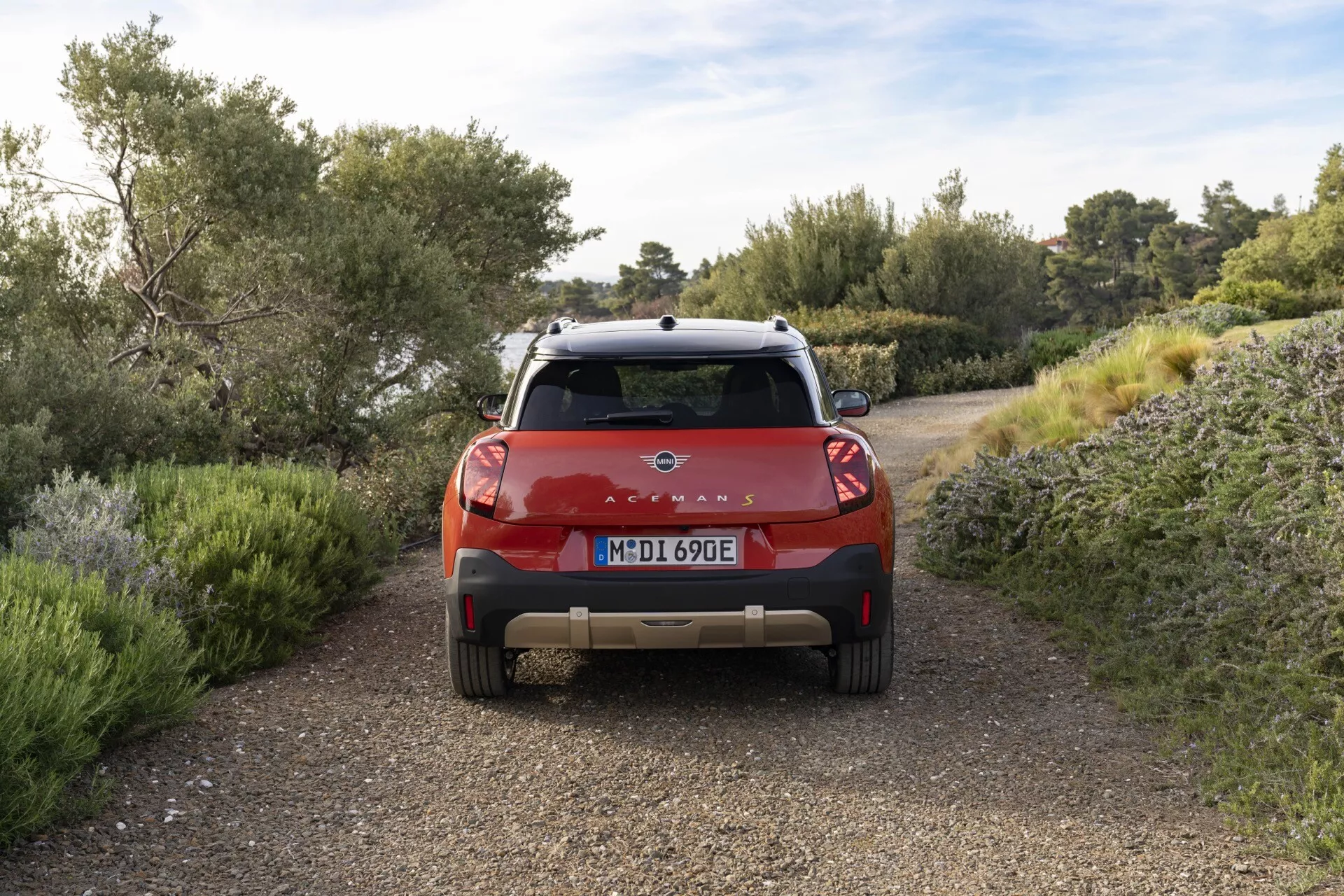 Modern Mini Aceman 2024 (JO5) rear-angle view highlighting LED tail lights, electric/hybrid badging, parking assistance sensors, rearview camera system, and roof rack on a dirt path with natural scenery