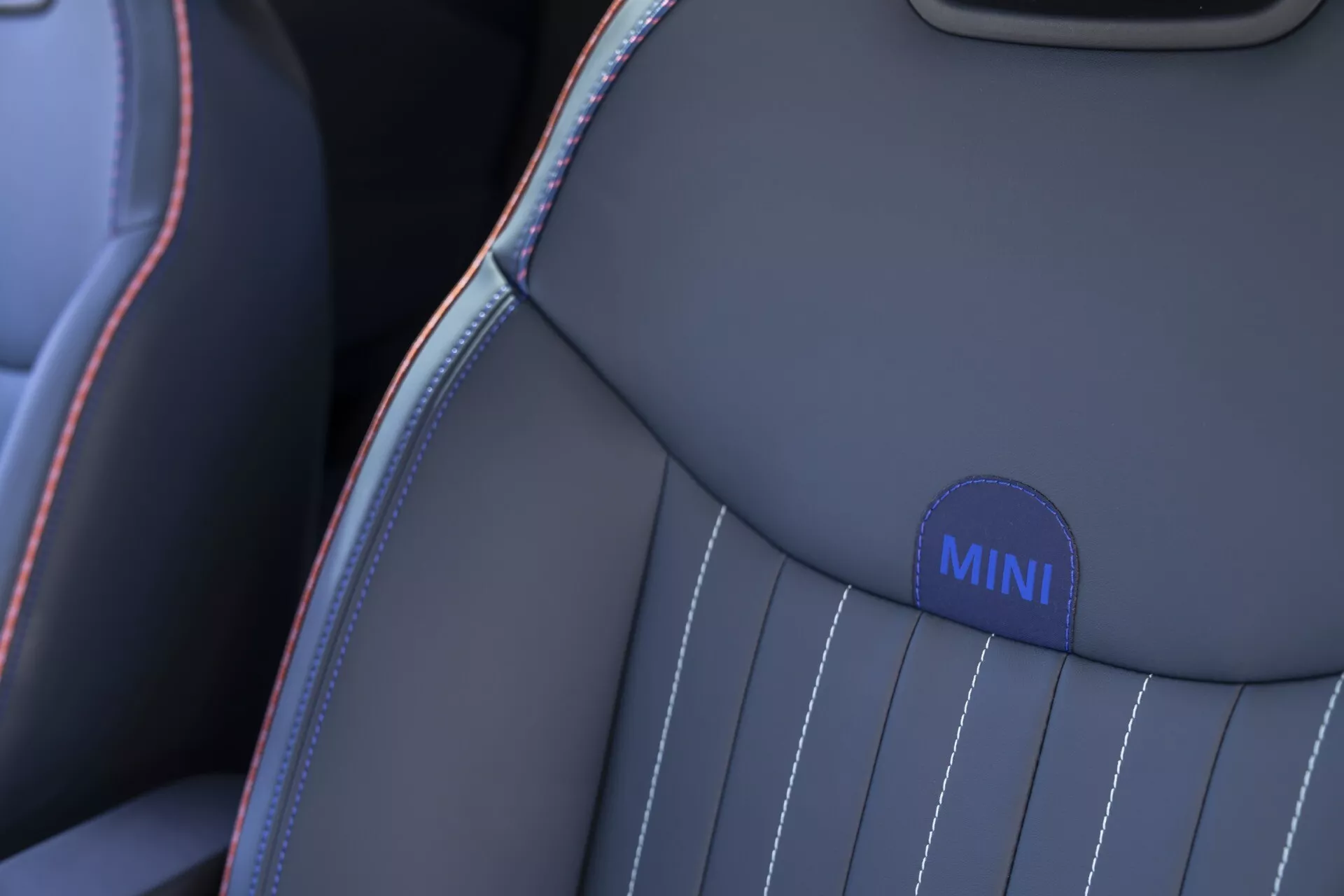Close-up of MINI Aceman 2024 car seat highlighting the upper shoulder with embroidered badge, contrast stitching, and vertical stripe design in grey and blue