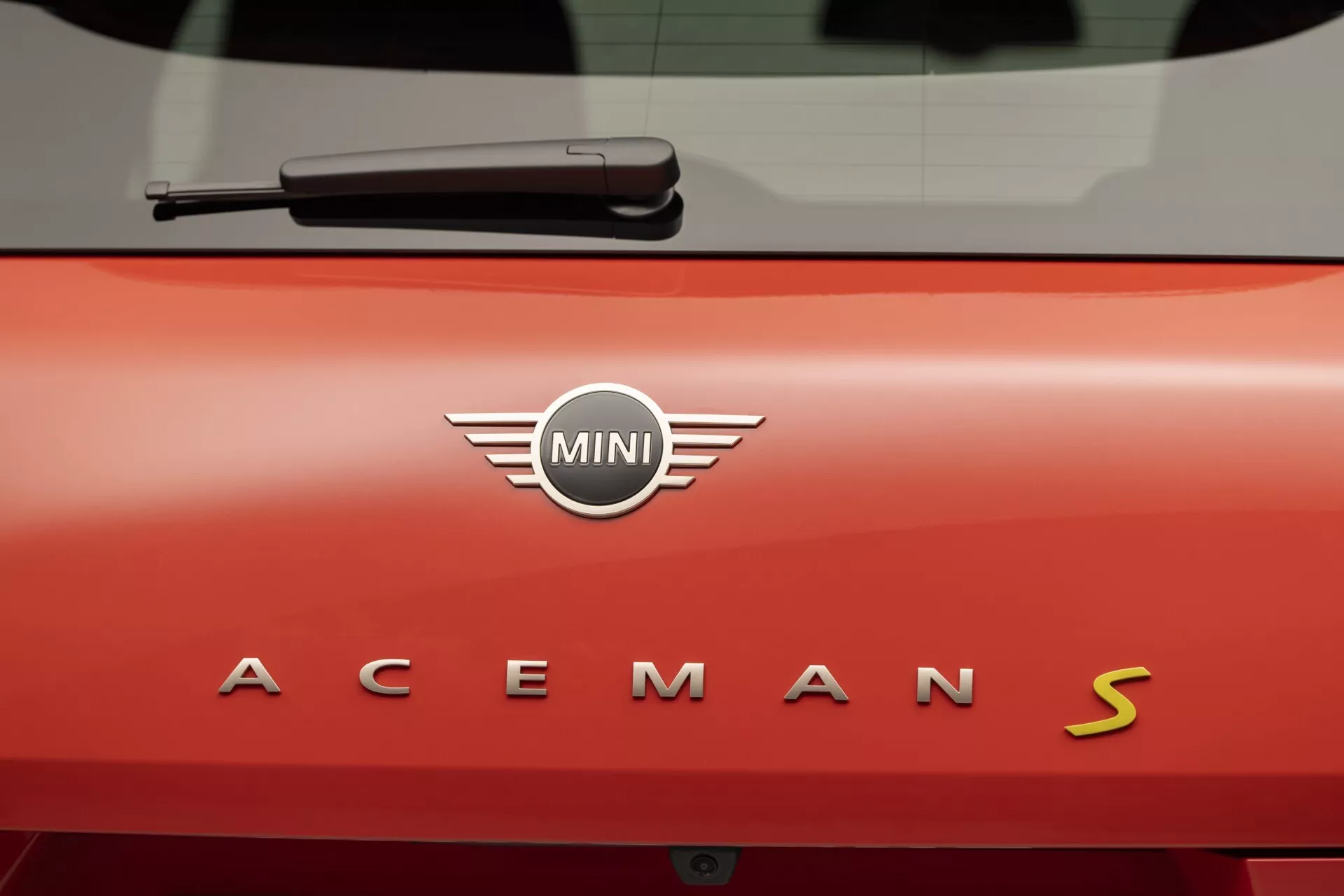 2024 MINI Aceman S close-up of vibrant red rear hatch with chrome brand logo and model designation under soft, indoor lighting