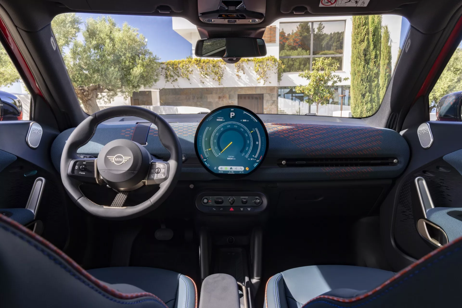 Interior view of the 2024 Mini Aceman (J05) showcasing driver's perspective with a modern three-spoke steering wheel, a fully digital instrument cluster, and a minimalist center console with advanced technologies