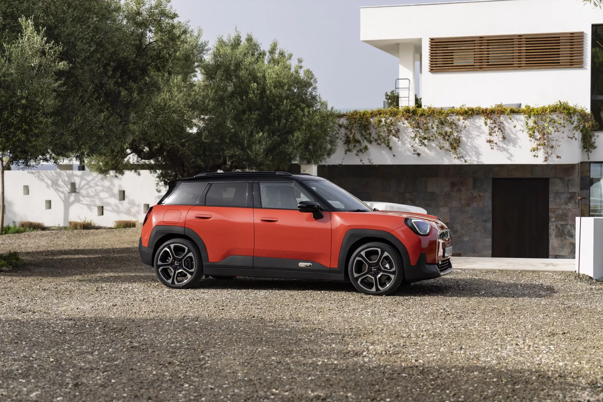 2024 Mini Aceman (J05) in dual-tone red and black showcasing side profile on gravel with large multi-spoke alloy wheels, tinted windows, and modern SUV features