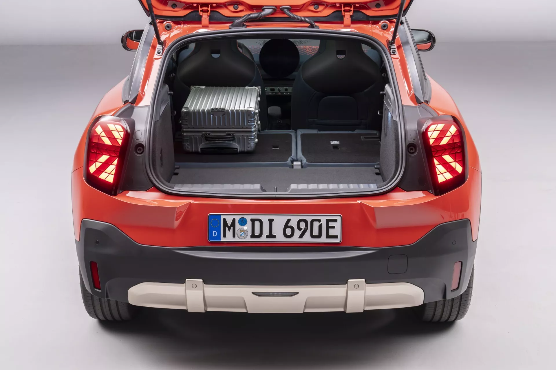 2024 Mini Aceman (JO5) high-angle rear view showing open trunk with power inverter, large cargo space, LED taillights, and parking sensors against a neutral studio background
