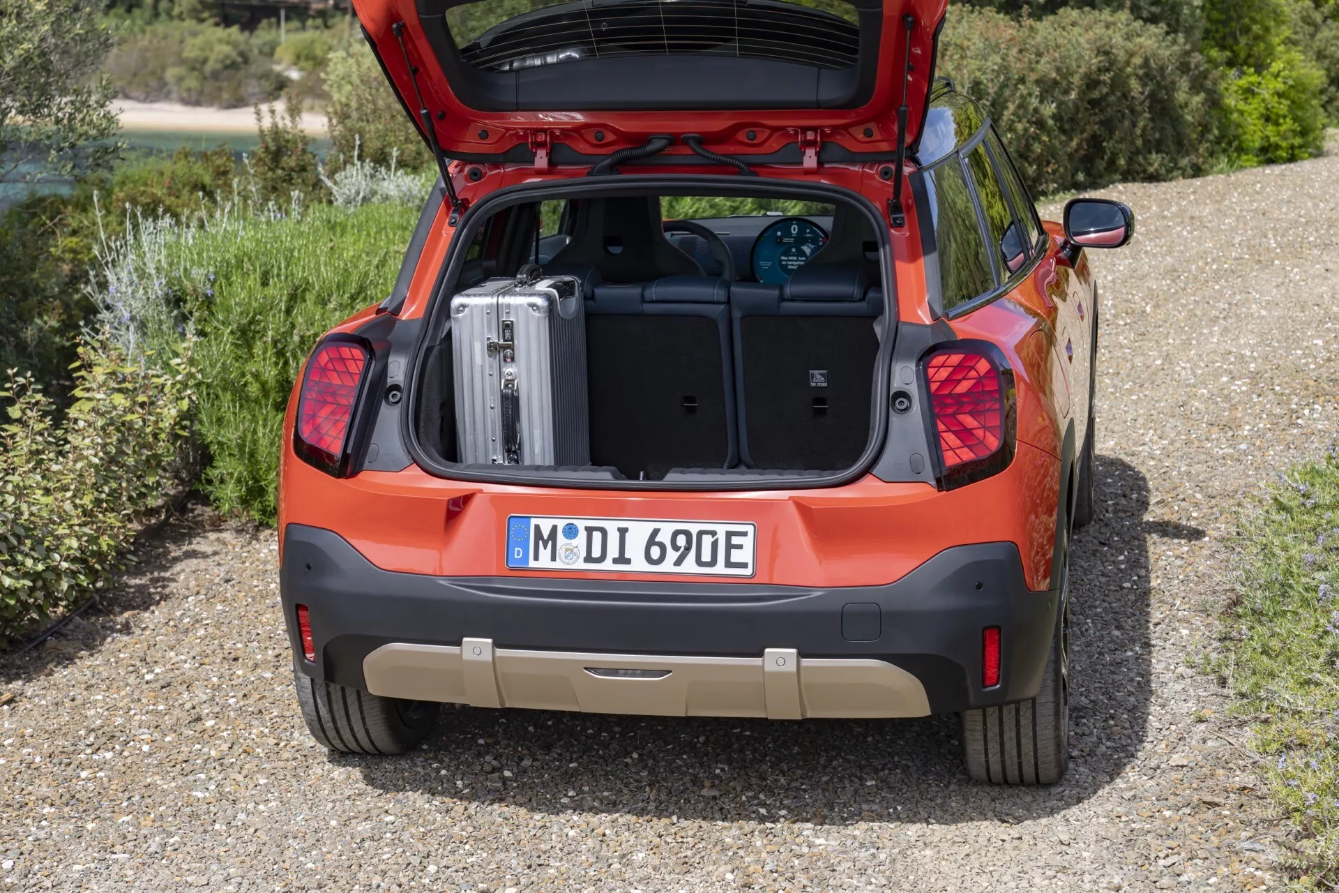 2024 Mini Aceman (J05) in red, showcasing rear design with an open hatch, loaded suitcase in flat trunk area, electric model indicators, and modern tail lights, set against a natural background