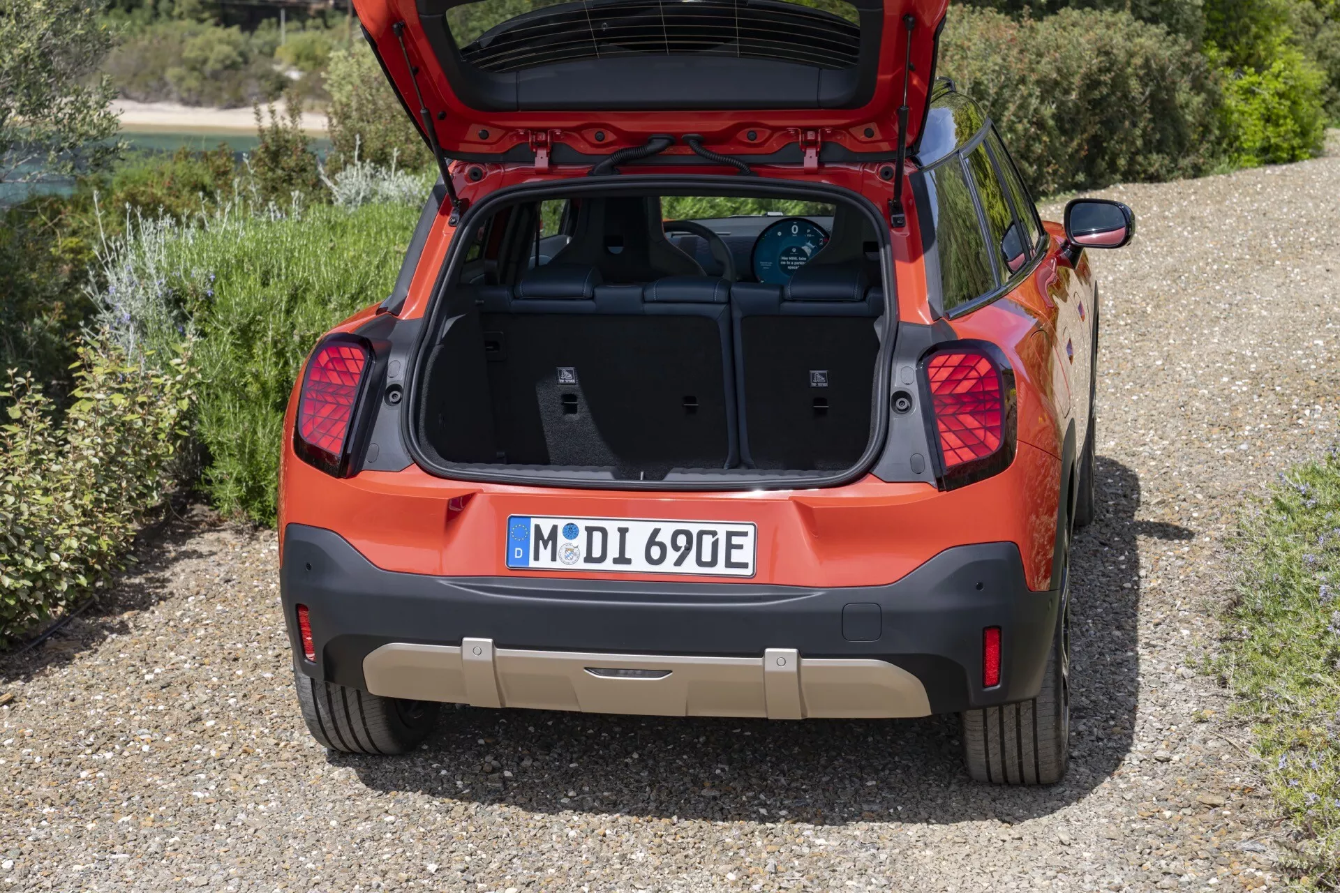 Rear view of a 2024 Mini Aceman (J05) compact crossover/SUV showcasing its open hatch and clean cargo space, modern LED tail lights, integrated low-profile rear spoiler, electric/hybrid badge, parking sensors/camera, and dual-tone paint with potential skid plate trim