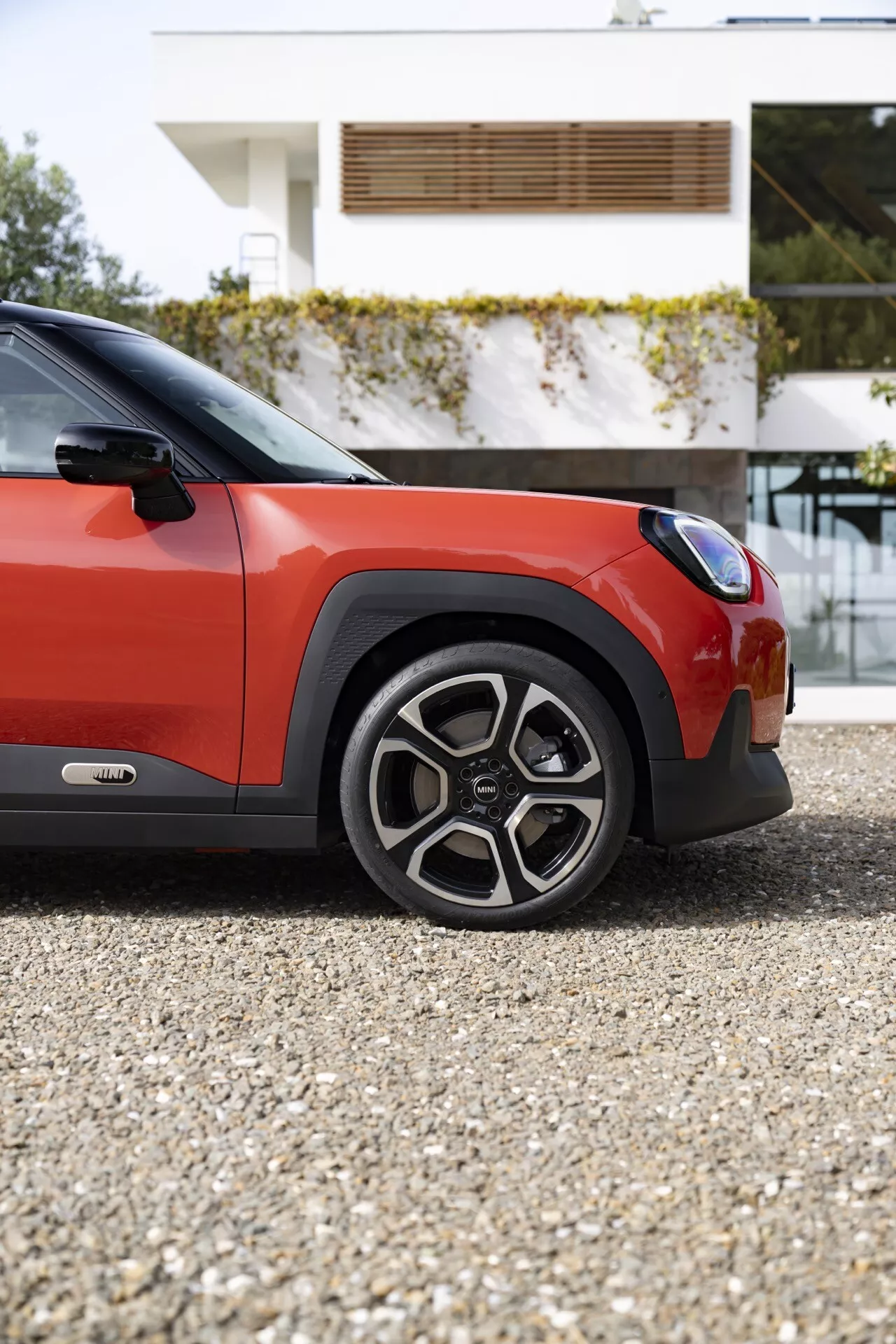 Close-up view of the 2024 MINI Aceman (JO5) showcasing the wheel, front fender, and door from a low angle, highlighting the car's two-tone color scheme and sporty, rugged design elements.