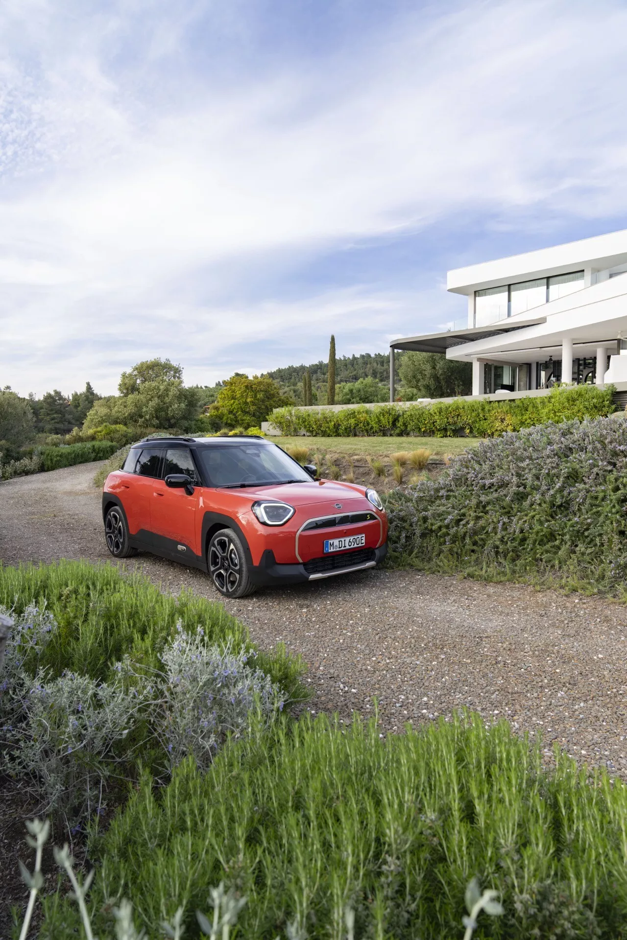 2024 Mini Aceman (J05) in a three-quarter front view, showcasing its sporty design, black-trimmed wheel arches, contrasting roof, and distinctive alloy wheels against an upscale residential backdrop