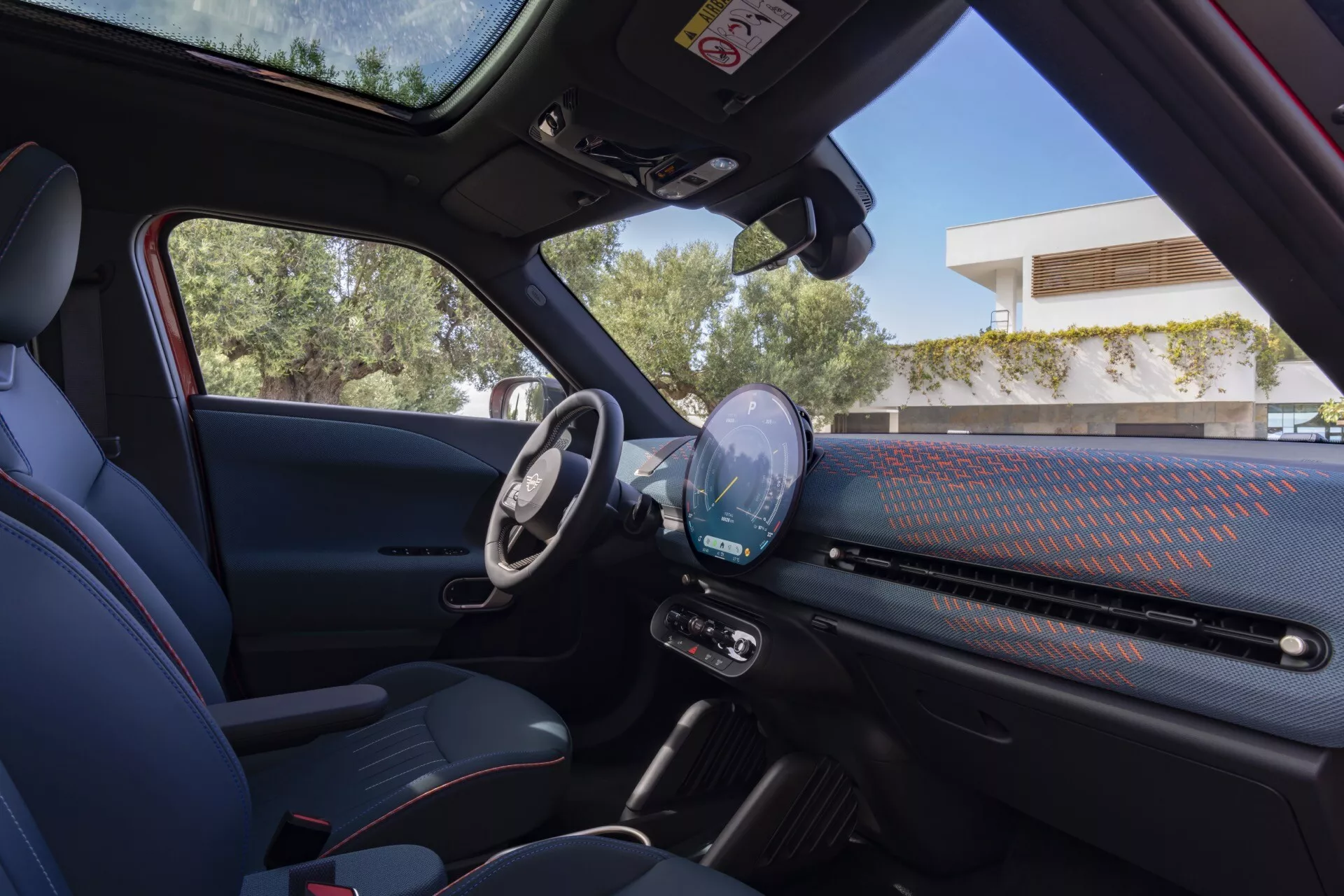 2024 Mini Aceman (J05) interior view from the back seat highlighting the driver's side with digital dashboard, multi-function steering wheel, and modern design elements