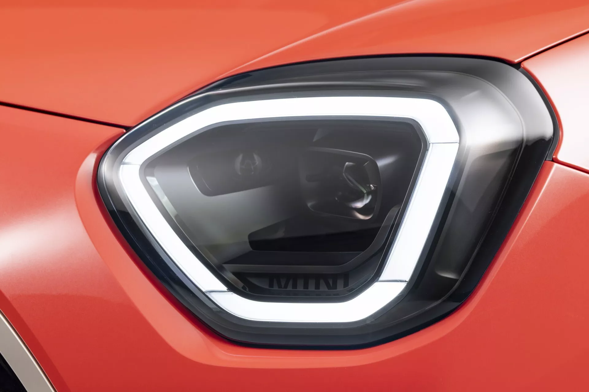 Close-up of the 2024 Mini Aceman (J05) left headlamp featuring LED technology, sharp angular lines, and onyx-black housing against a bright red bodywork