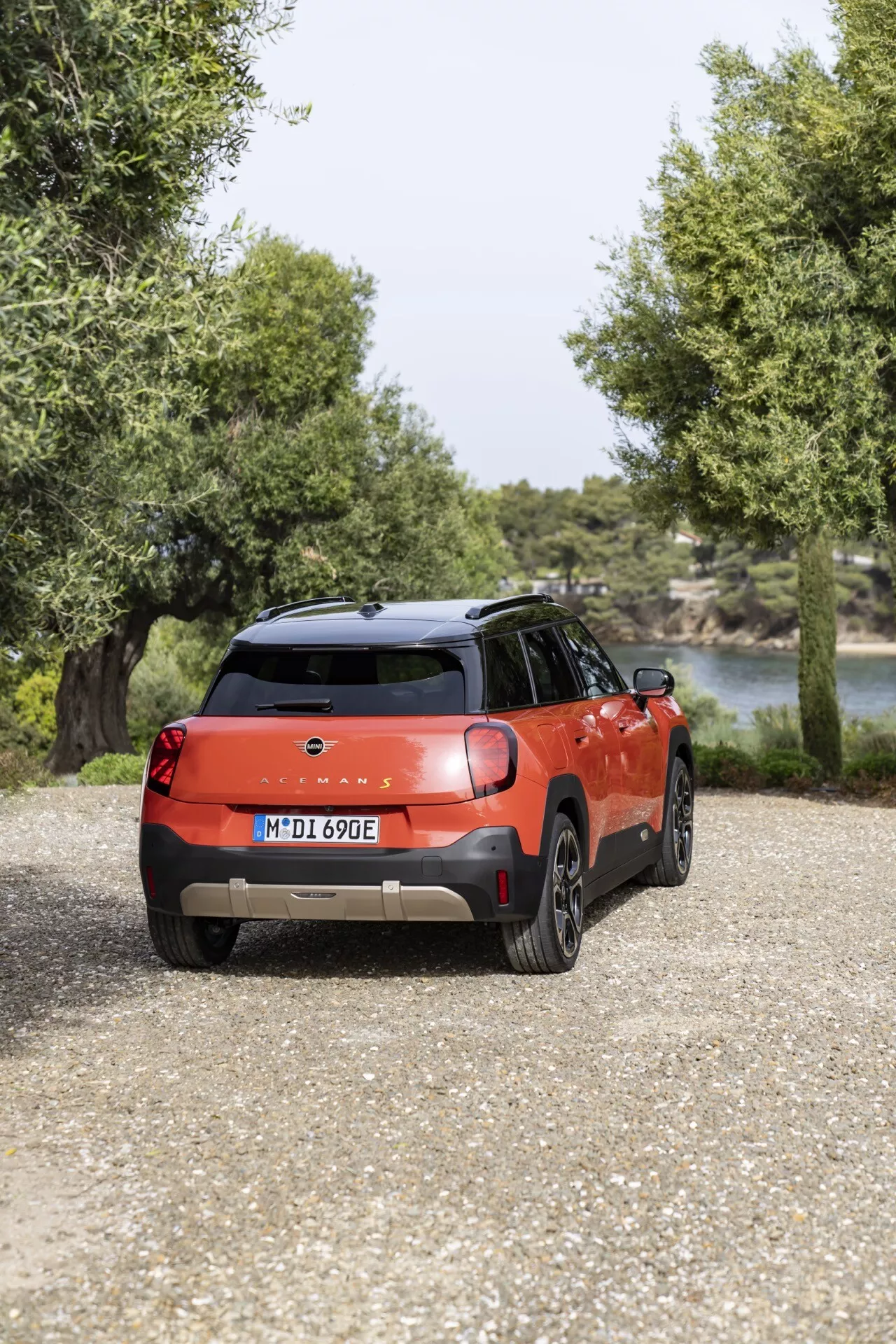 Rear-view of a 2024 Mini Aceman compact SUV in vibrant red with black roof, showcasing LED lights, alloy wheels, and parked in a Mediterranean setting