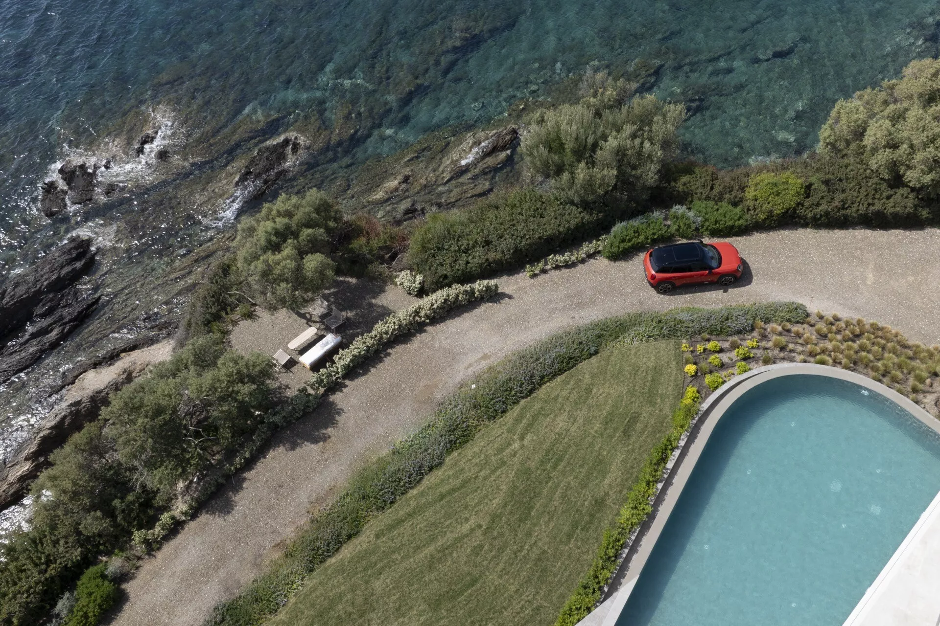 2024 Mini Aceman (J05) in red, featuring a high-angle aerial view parked next to a swimming pool, showcasing its sleek, sporty design and glossy finish within a luxurious setting