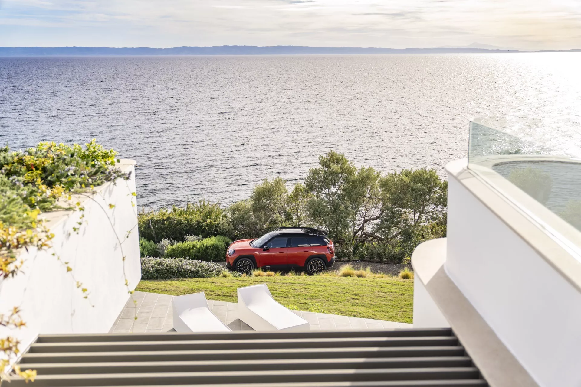 2024 Mini Aceman (J05) parked on grass near coast with modern structural background and descending staircase, highlighting red sleek design, rear LED lights, and alloy wheels
