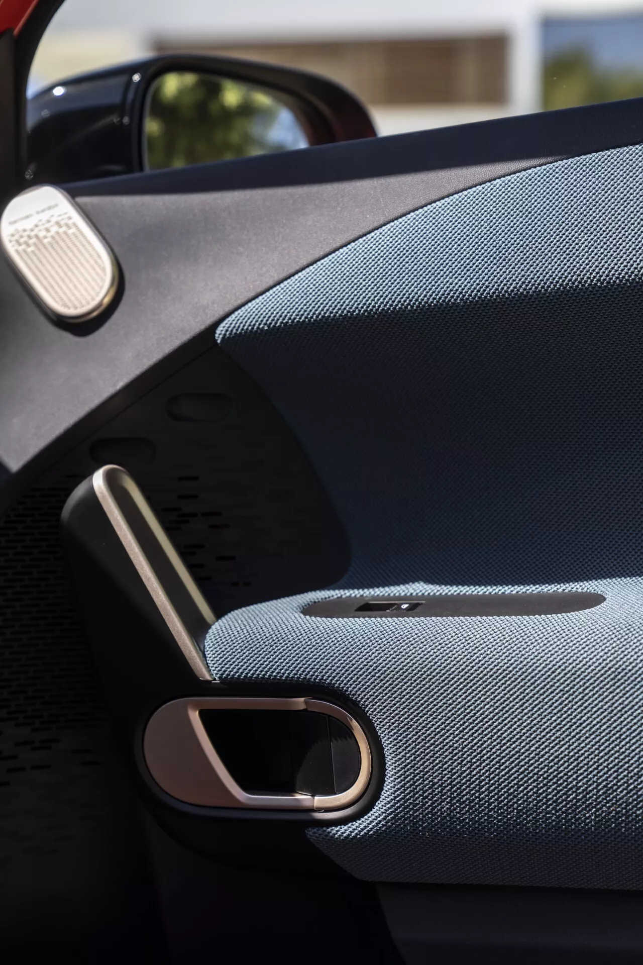 Close-up view of a 2024 Mini Aceman (J05) car door interior, showcasing a luxurious armrest, sleek metal door handle, integrated premium speaker grille, and high-quality materials aimed at enhancing user comfort and vehicle aesthetics