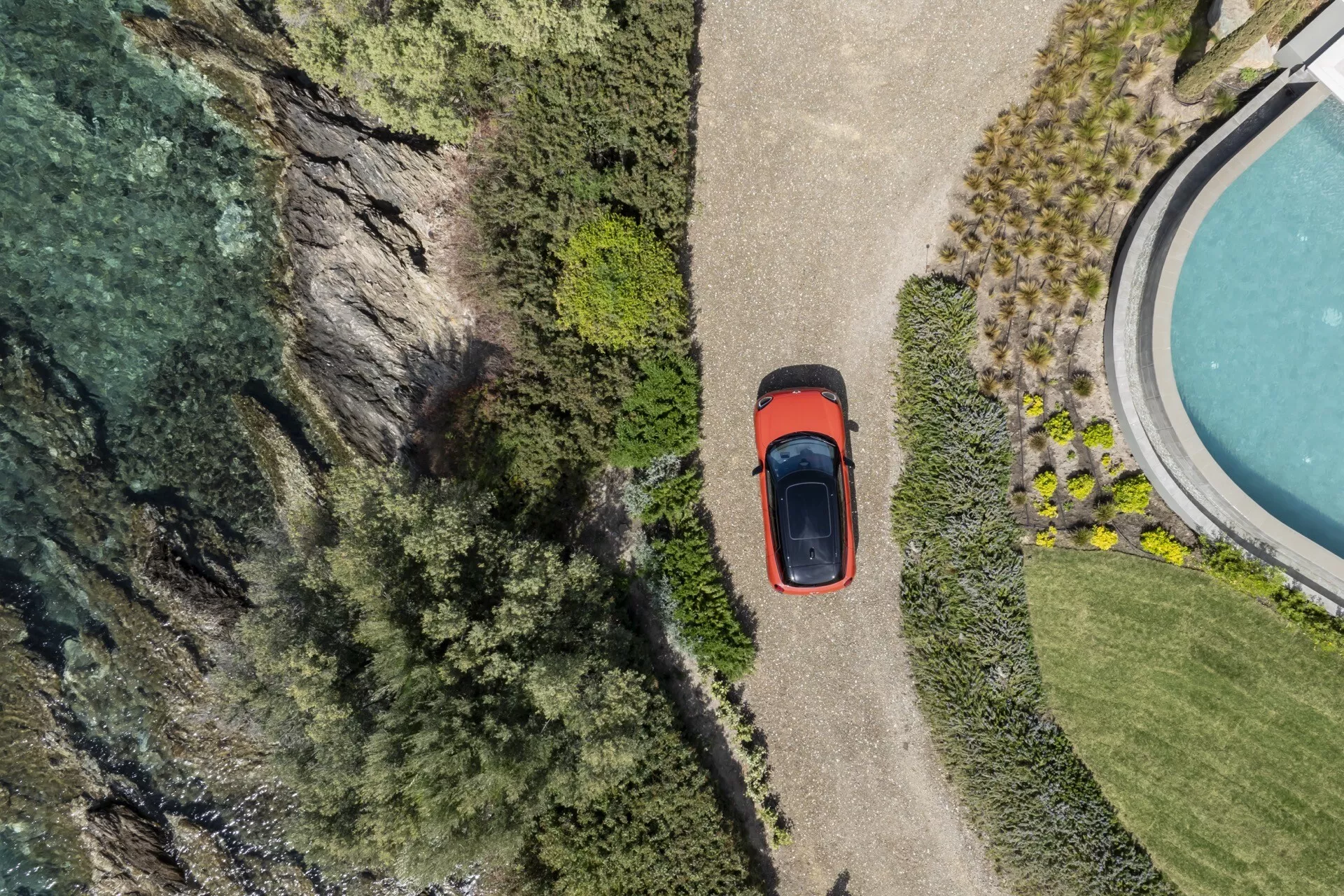 Aerial view of Mini Aceman 2024 (J05) showcasing its roof, hood, trunk, and partial side profile parked near a cliff and water body, surrounded by lush vegetation, highlighting the car's sunroof feature
