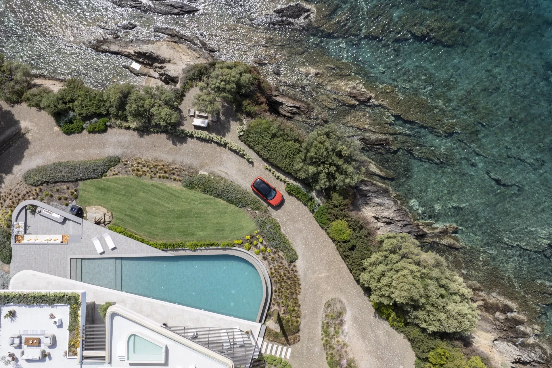 Aerial view of a red Mini Aceman 2024 (J05) parked on a private driveway near the coast, surrounded by natural scenery and luxury amenities