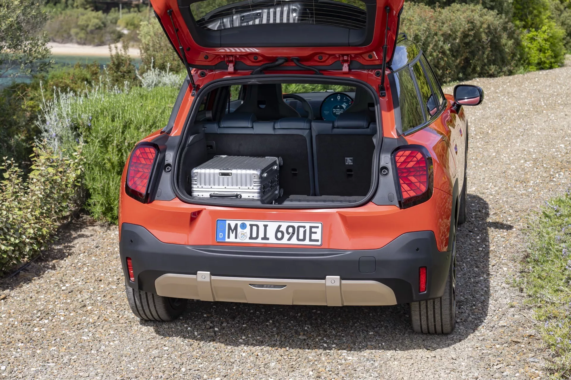 Rear view of the Mini Aceman 2024 (J05) showcasing spacious trunk, electric/hybrid powertrain hints, and vibrant orange finish in an outdoor setting