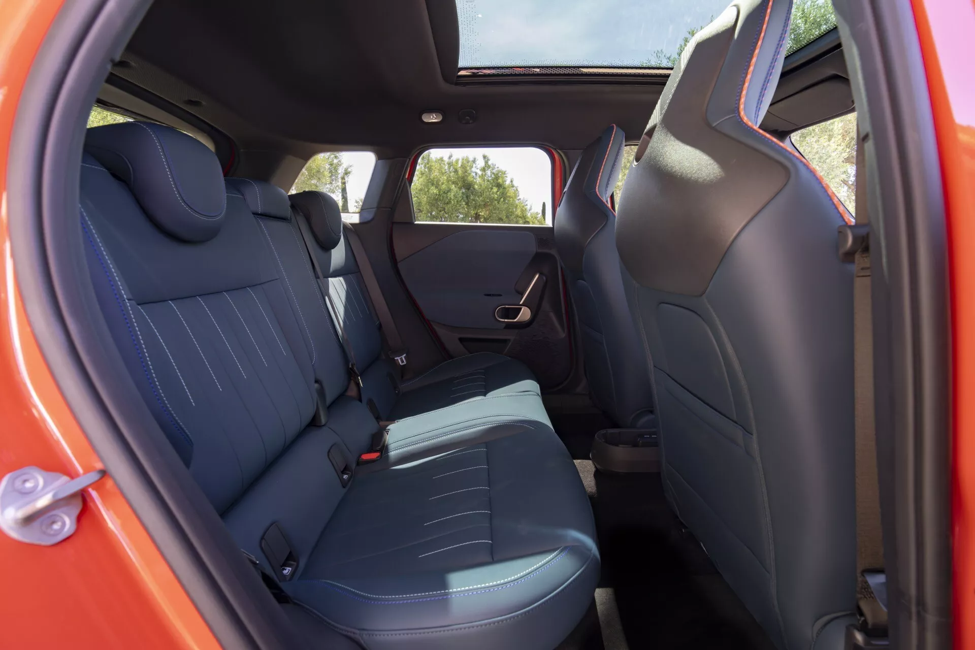 2024 MINI Aceman (J05) interior view showcasing the rear seats through the open passenger door from an external low to mid angle, featuring dark upholstery with blue accents, integrated headrests, and modern design elements