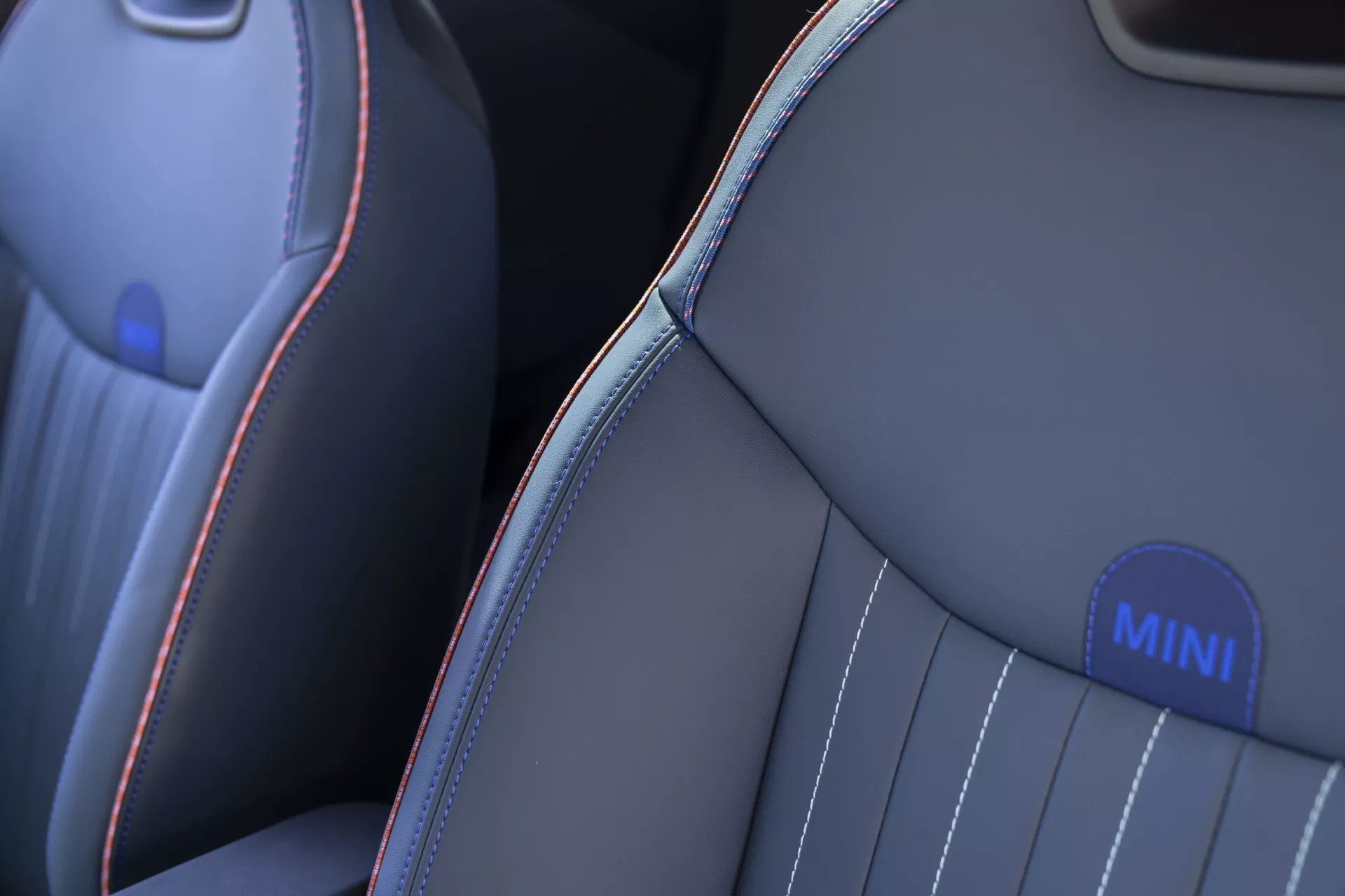 Close-up view of the MINI Aceman 2024 (J05) front seat showcasing premium dark grey or black upholstery with contrasting red and light blue stitching, vertical channeling for comfort, and a branded MINI emblem on the side bolster