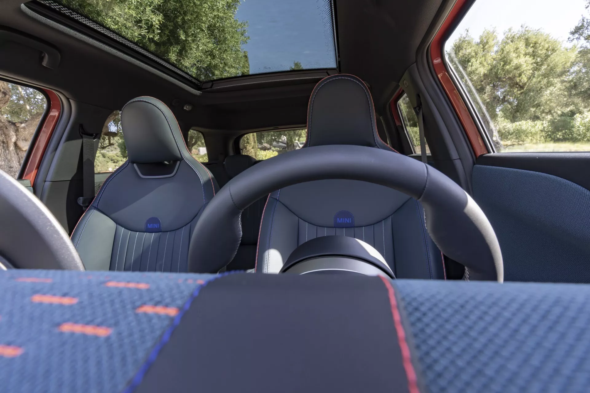 Interior view of 2024 Mini Aceman (J05) showing front seats, steering wheel, and panoramic roof from rear seat perspective, highlighting upholstery design and modern features