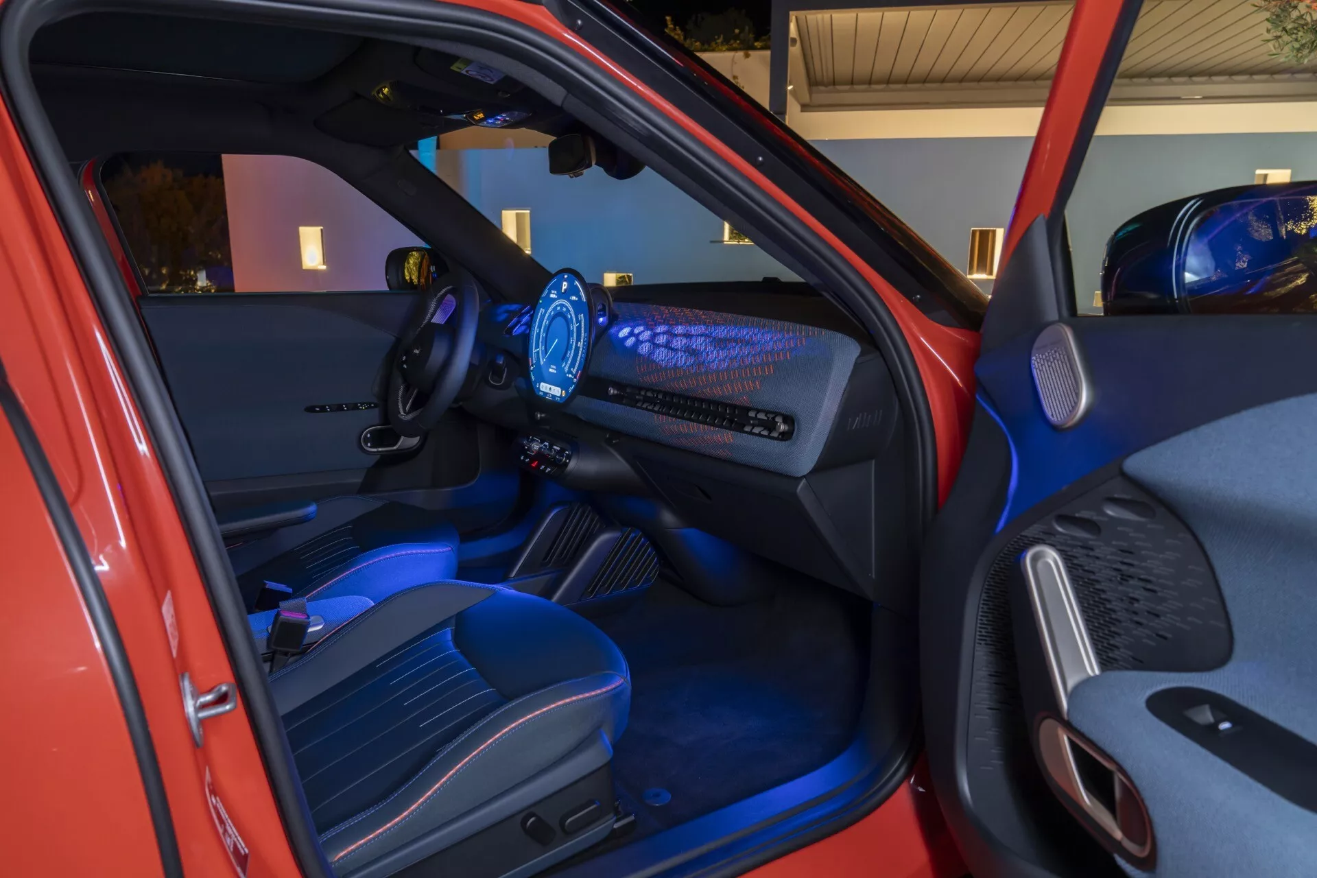 Interior view of the 2024 Mini Aceman (JO5) showcasing the driver's side door, ergonomic steering wheel, digital dashboard, and the front passenger area with ambient blue lighting and advanced technology features