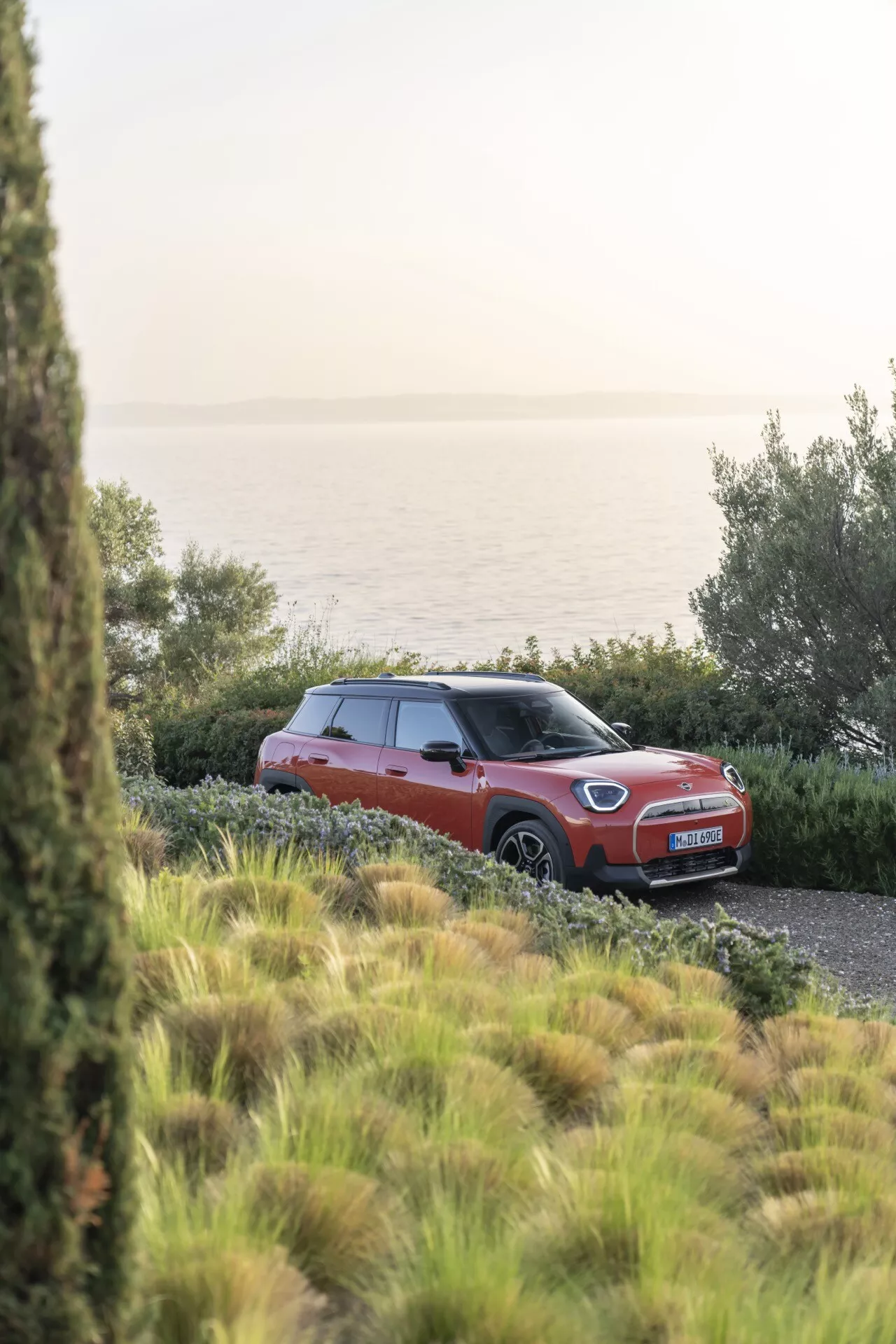 2024 Mini Aceman (J05) parked outdoors in natural setting during daylight, showcasing a red or orange body with contrasting roof, alloy wheels, and a three-quarter front view