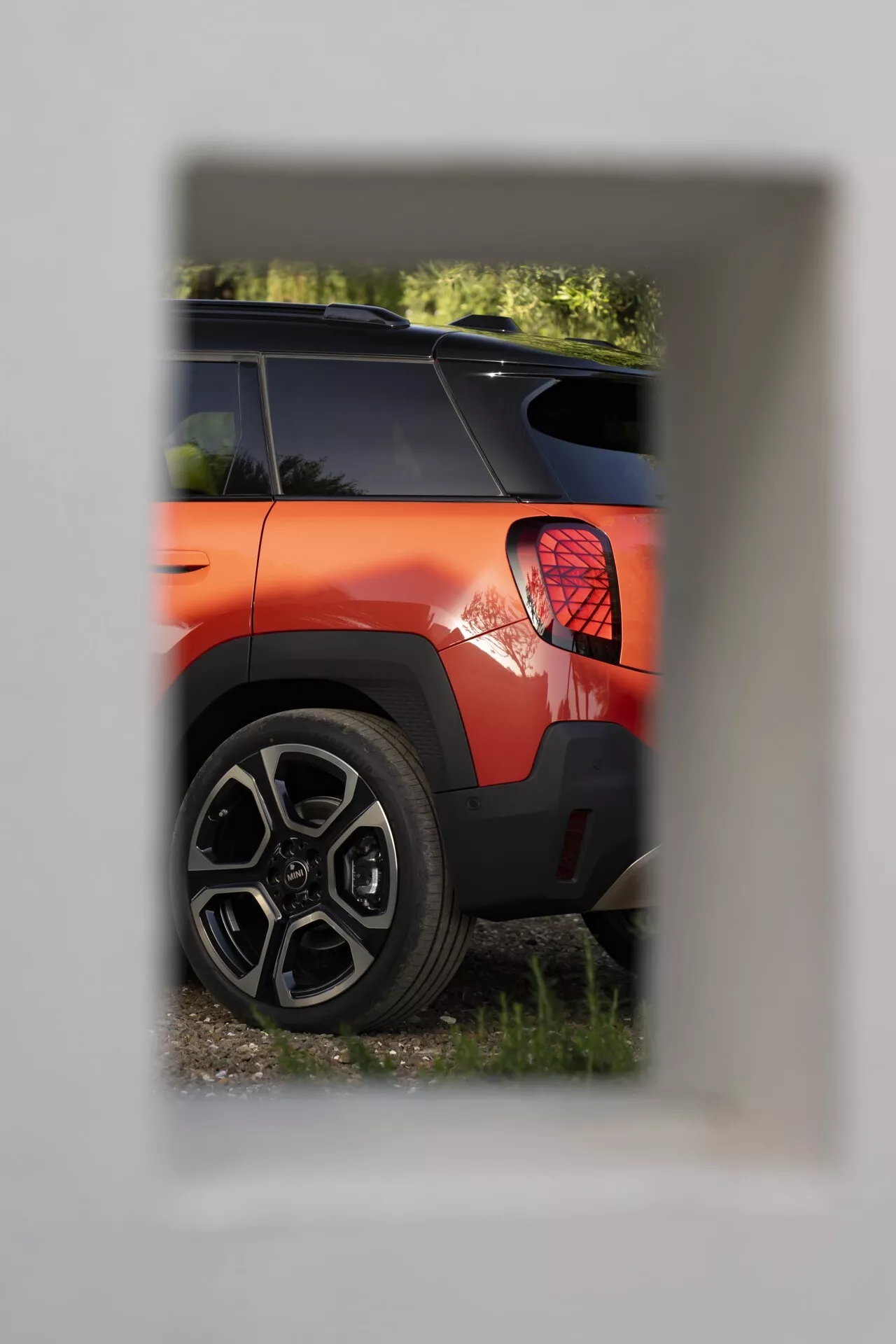 Partial view of a 2024 Mini Aceman (J05) in bright orange with a focus on the rear quarter section, featuring a circular LED tail light and sporty multi-spoke alloy wheel