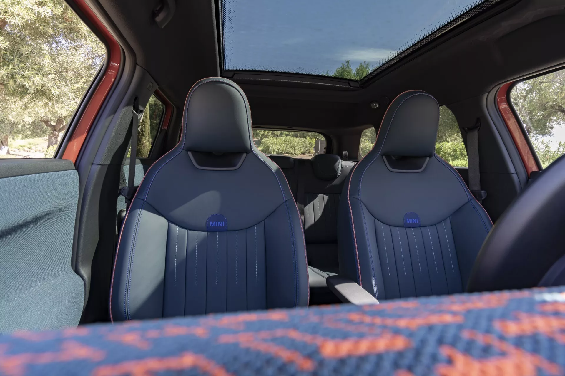 Interior view of the Mini Aceman 2024 (J05) from the second-row, showcasing front bucket-style seats and dashboard through a natural light-filled cabin with a panoramic sunroof.