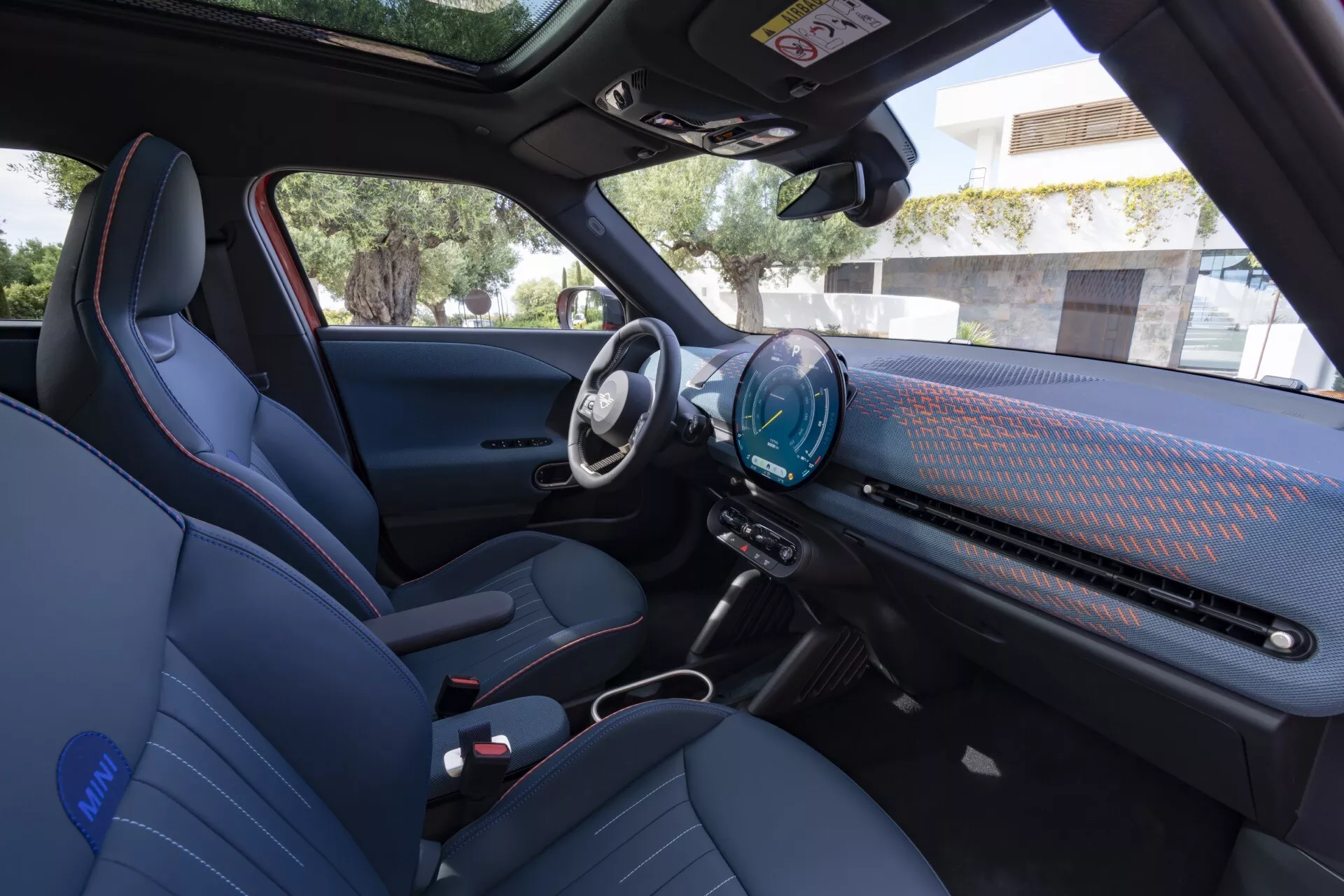 2024 Mini Aceman (J05) interior view from the front passenger door showcasing driver's seat, passenger's seat, steering wheel, dashboard, and center console with advanced features and modern design