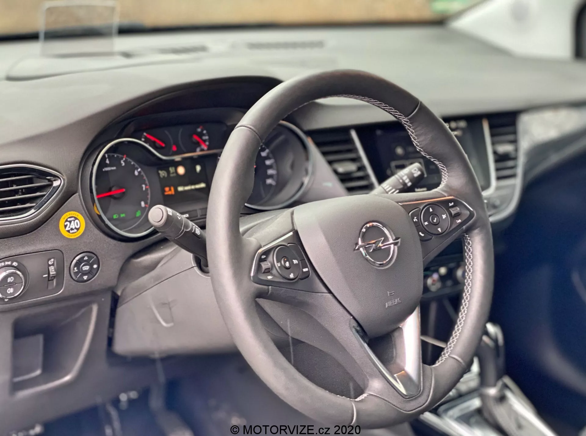 This image shows the interior of a 2021 Opel Crossland from the driver's perspective, focusing on the steering wheel and dashboard. The steering wheel, which is centrally-located, includes control buttons on both spokes for features such as audio control, hands-free phone operation, and cruise control. Behind the steering wheel is a partial view of the instrument cluster with the tachometer and various warning indicators. The dashboard includes air vents and a partially obscured infotainment system, all suggesting a modern and technologically-equipped interior design.
