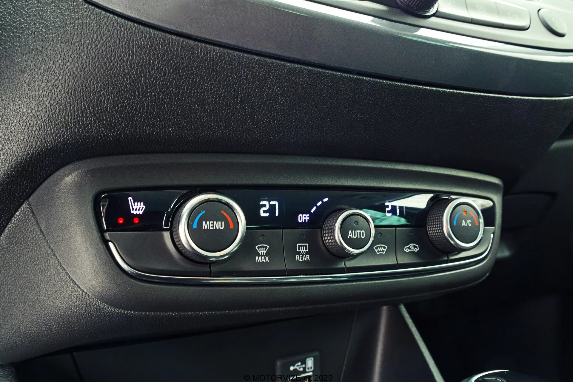 Close-up of the climate control panel in a car interior, featuring a sleek, modern design with black surfaces, silver accents, and clear white labeling. The frontal, slightly downward perspective showcases the control buttons and dials. The left dial with a red LED and '27' displayed controls the driver's temperature. The 'MENU' button with a fan icon allows for fan settings customization. Smaller 'OFF' button likely turns off the system. 'MAX' fan and 'REAR' defrost buttons, 'AUTO' for automatic climate control, and the right dial with a blue LED for passenger temperature complete the advanced, functional design.