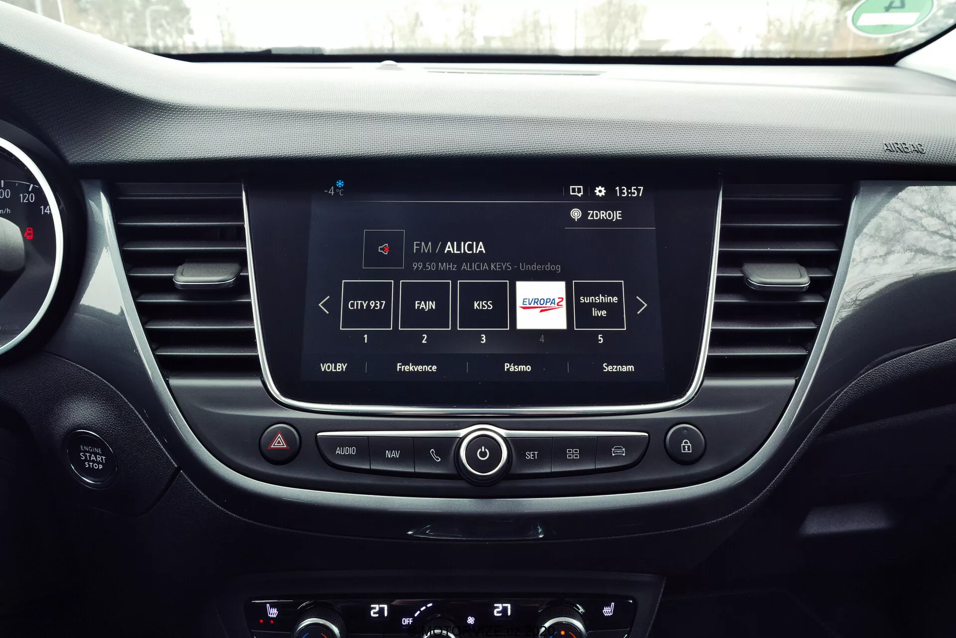 Interior view of a 2021 Opel Crossland focusing on the central dashboard area, featuring the infotainment system displaying FM radio functions with station information and sound settings, as well as physical buttons and knobs for audio and climate control.