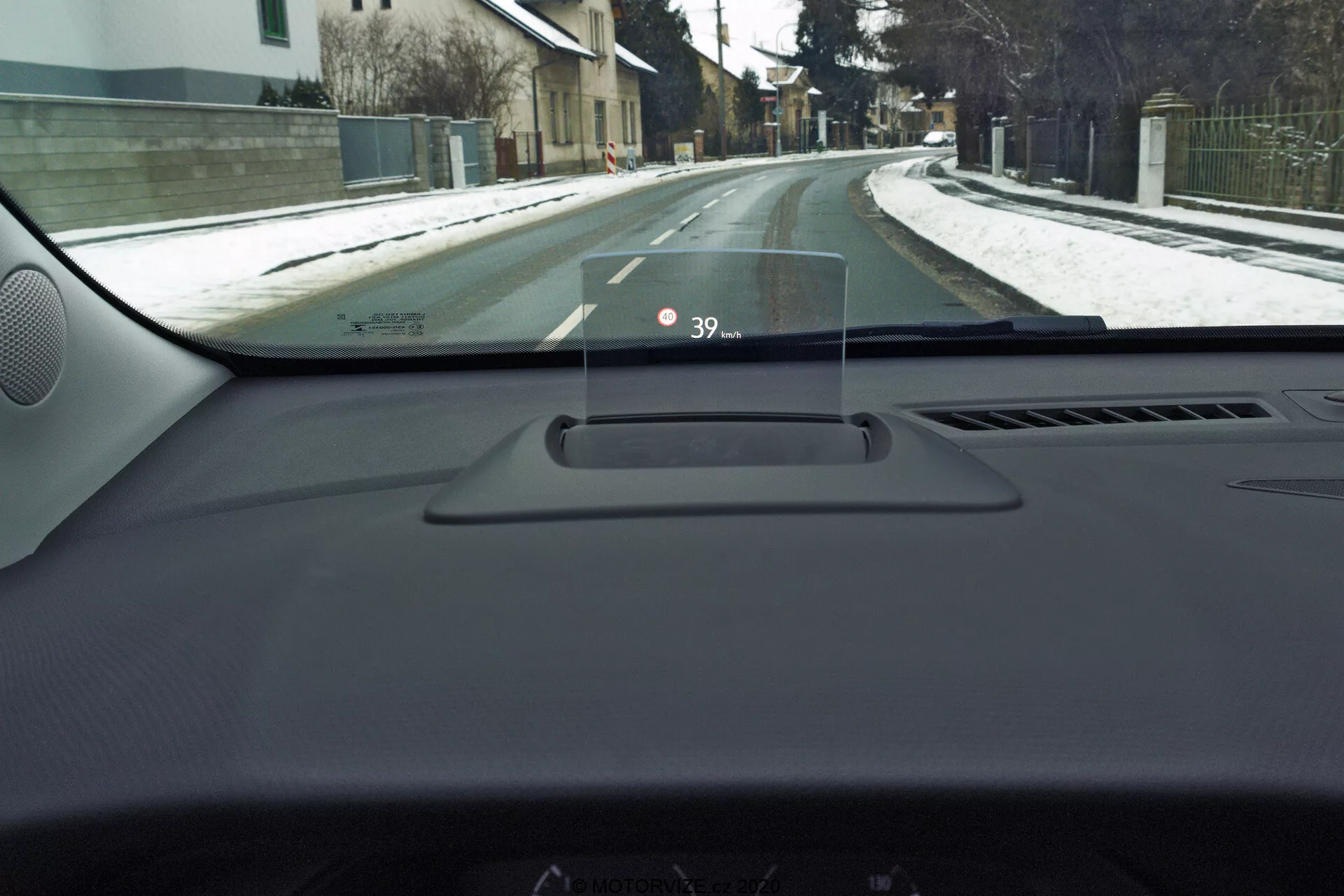 Driver's perspective interior view inside a 2021 Opel Crossland, highlighting the Heads-Up Display (HUD) on the dashboard showing speed '39'. The view includes the dashboard, driver's side door edge, A-pillar, and a partial residential street scene with snow, suggesting winter conditions.