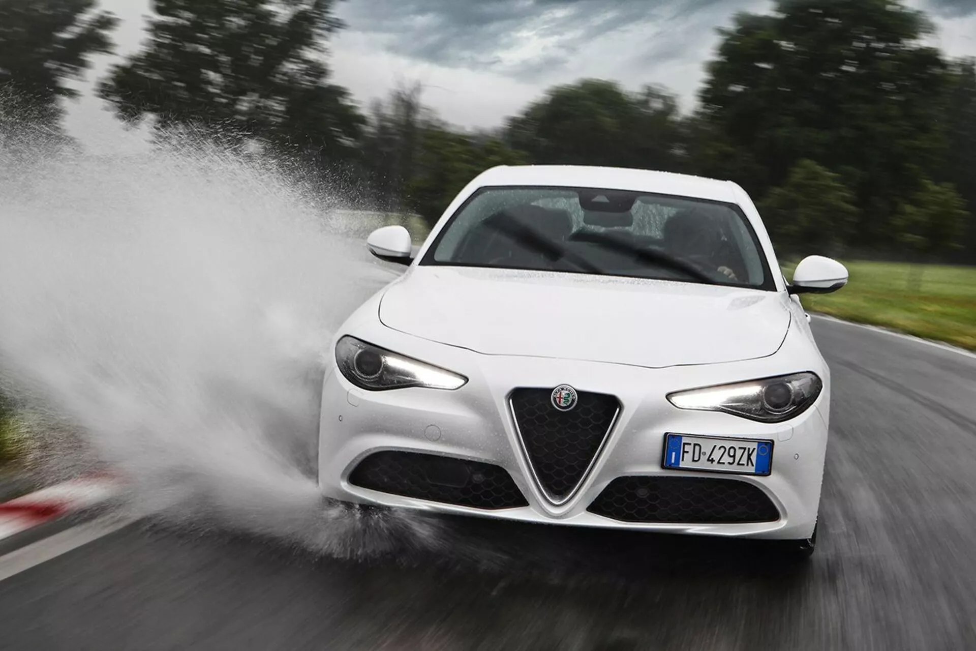 White 2016 Alfa Romeo Giulia sports car speeding through water, causing a splash, in a three-quarter front view highlighting its LED headlights, distinctive front grille, sleek side mirrors, and aerodynamic body lines