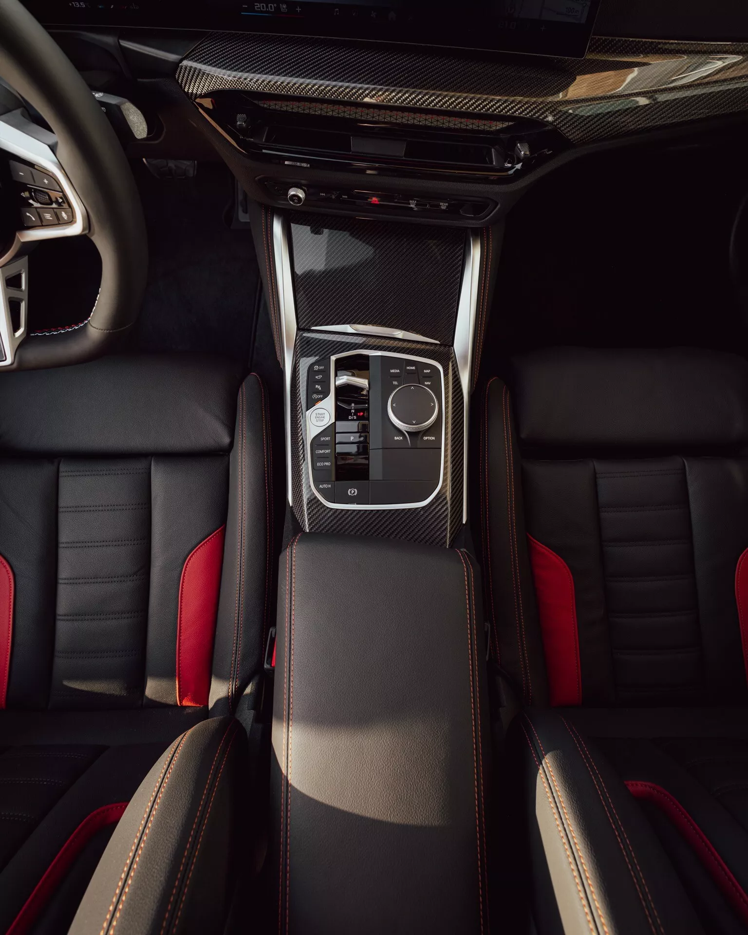 Overhead interior view of BMW 2-Series 2024 (G42-G87 facelift) showing central console with carbon fiber trim, sleek gear shift lever, electronic touchpad, climatic controls, sporty front leather seats with contrast stitching, and partial view of the rear seats.