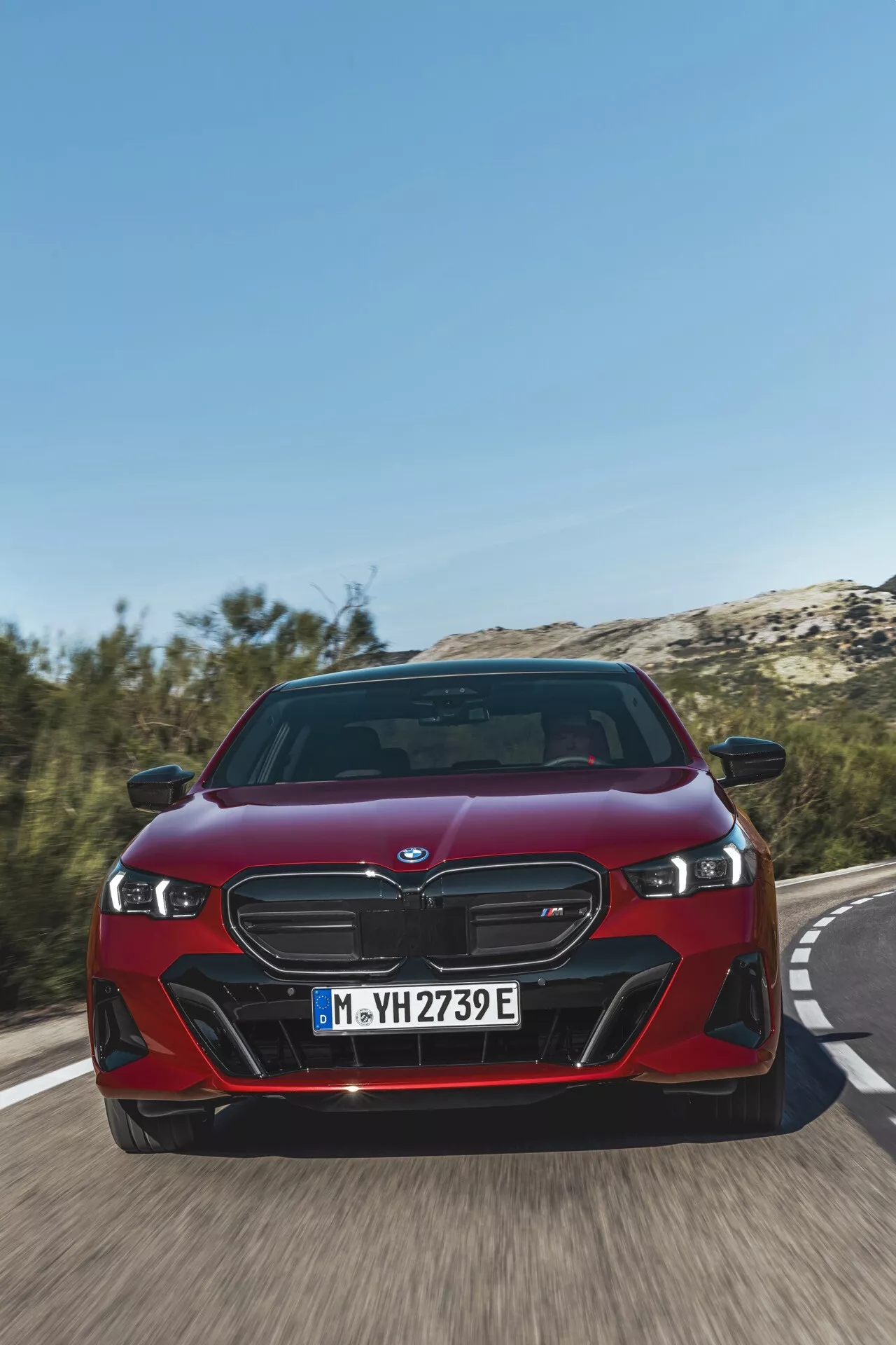 2023 BMW 5 Series (G60-G61) in red, showcasing its distinctive twin-kidney grille, LED headlights, and dynamic front fascia from a low front angle on a roadway, highlighting the vehicle's speed and advanced electrified iPerformance features