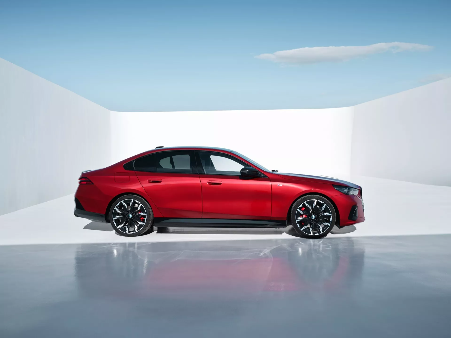 2023 BMW 5 Series (G60-G61) red four-door sedan in studio setting with reflective floor, showcasing side-profile, modern design and advanced features