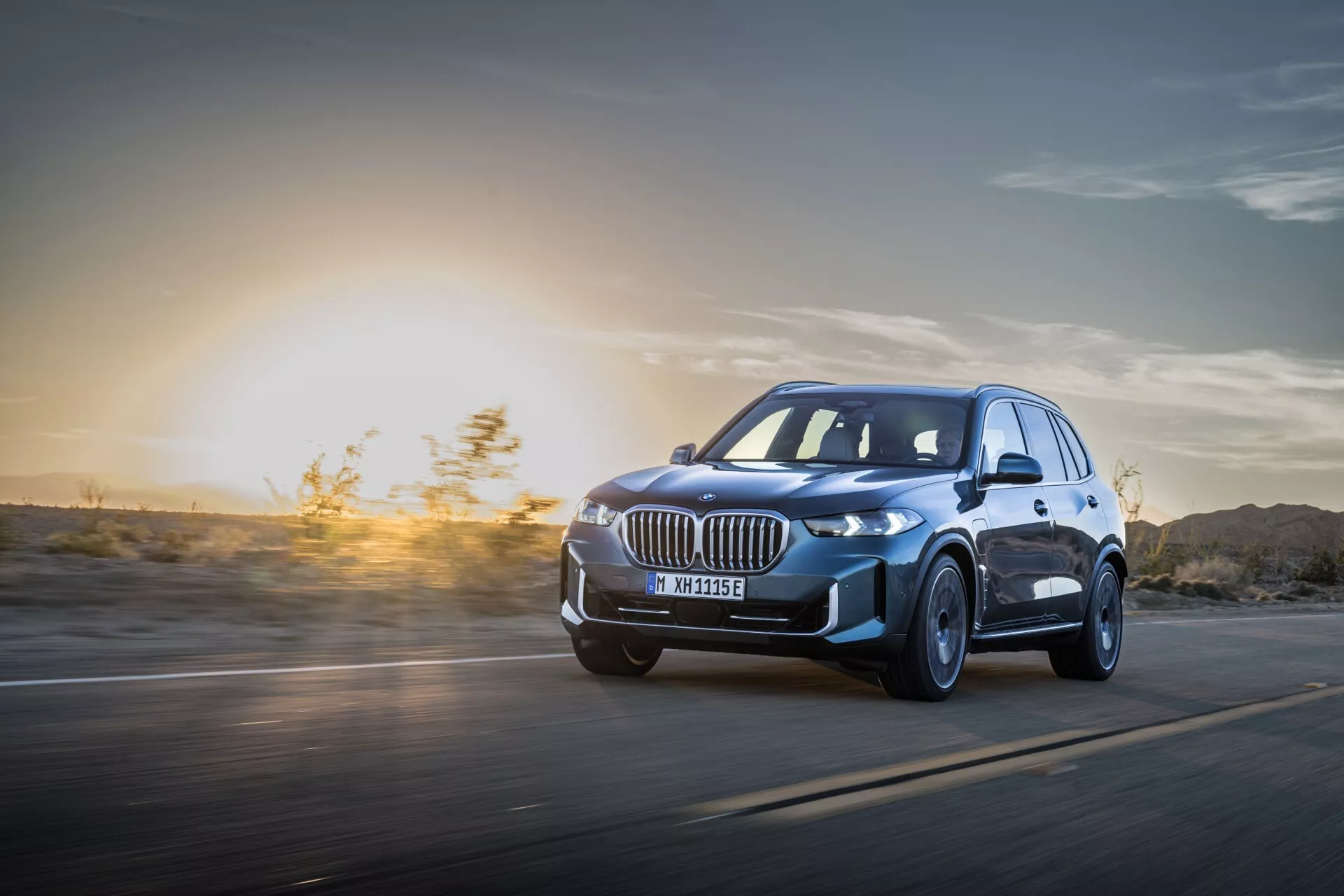 2023 BMW X5 (G05-F95 Facelift) in Motion: A Dynamic Low-Angle Three-Quarter View Highlighting LED Headlights, Alloy Wheels, and Aerodynamic Design Against a Sunset