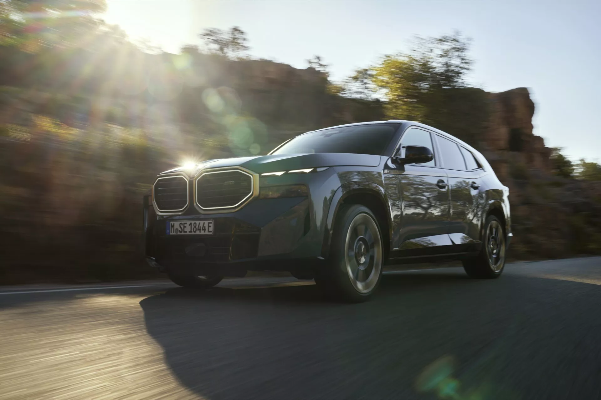 Dynamic view of a 2023 BMW XM (G09) in motion, showcasing the front left quarter, grille, LED headlights, and wheel design under natural lighting conditions