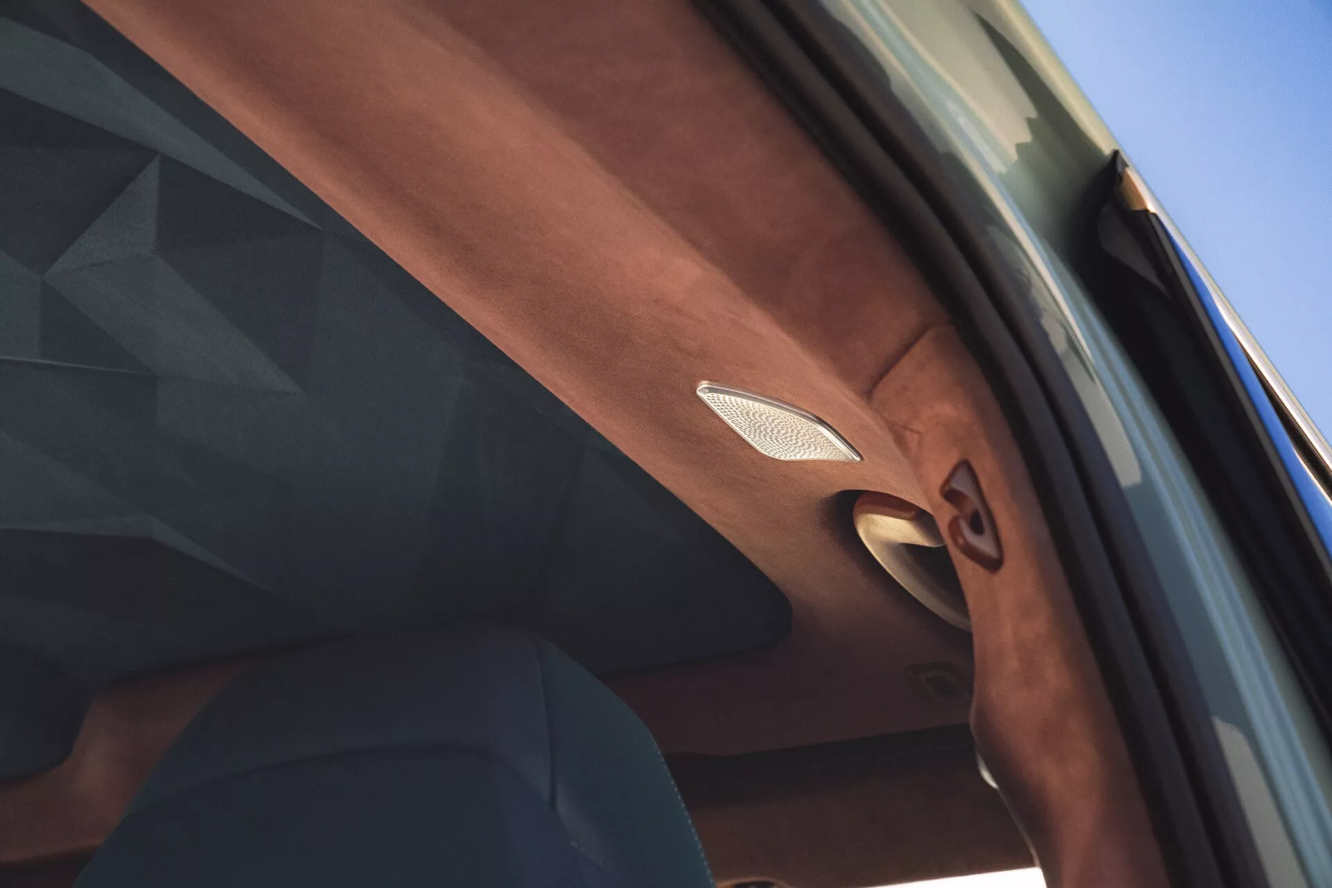 Close-up view inside a BMW XM 2023, focusing on high-detail of the passenger's side pillar featuring a premium speaker grille with metallic trim and intricate texture details, hinting at luxury interior design.
