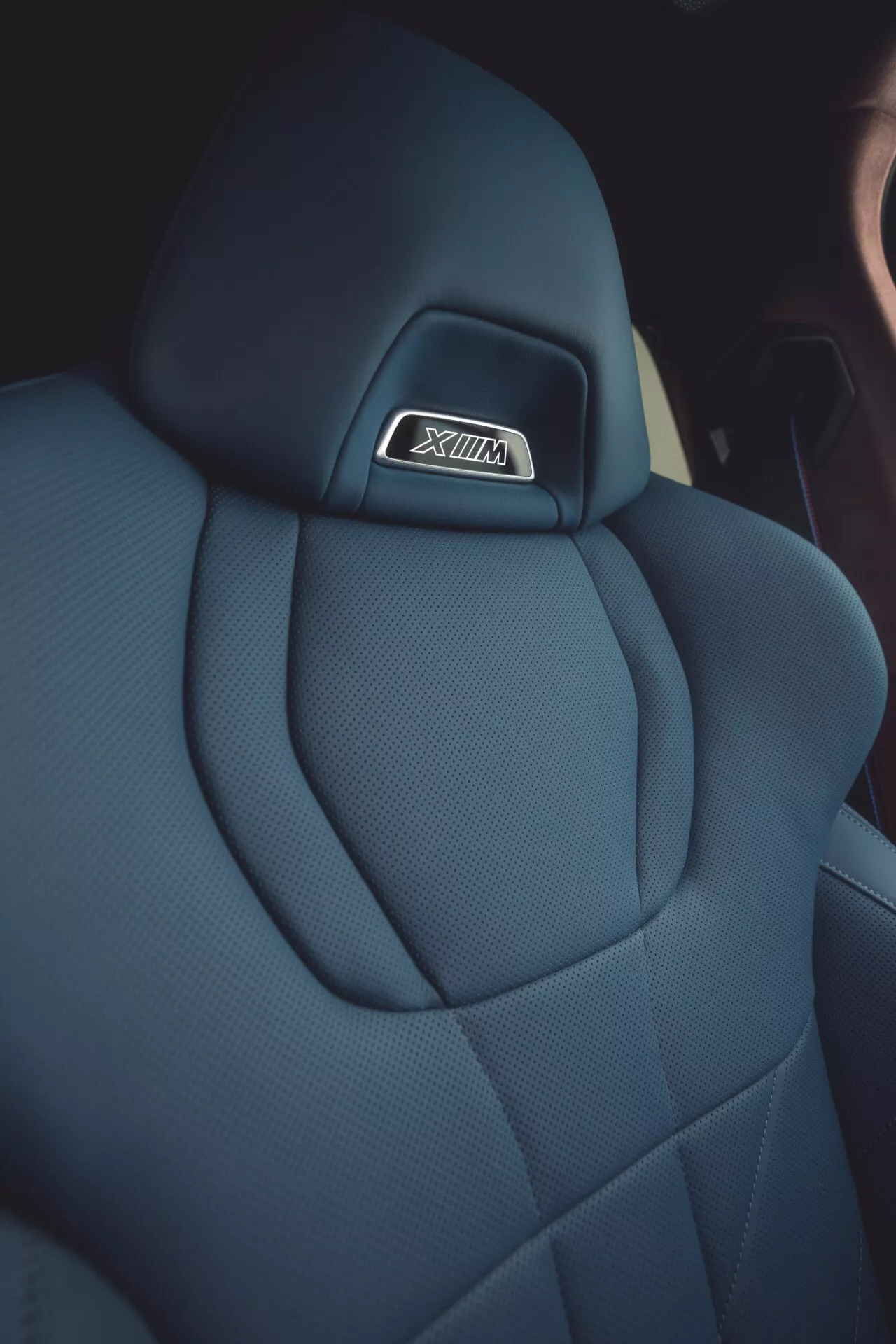 Close-up view of the BMW XM 2023 (G09) car seat showcasing the premium dark fabric headrest with SRT logo, diamond quilt pattern stitching, and ergonomic design emphasizing luxury and performance.