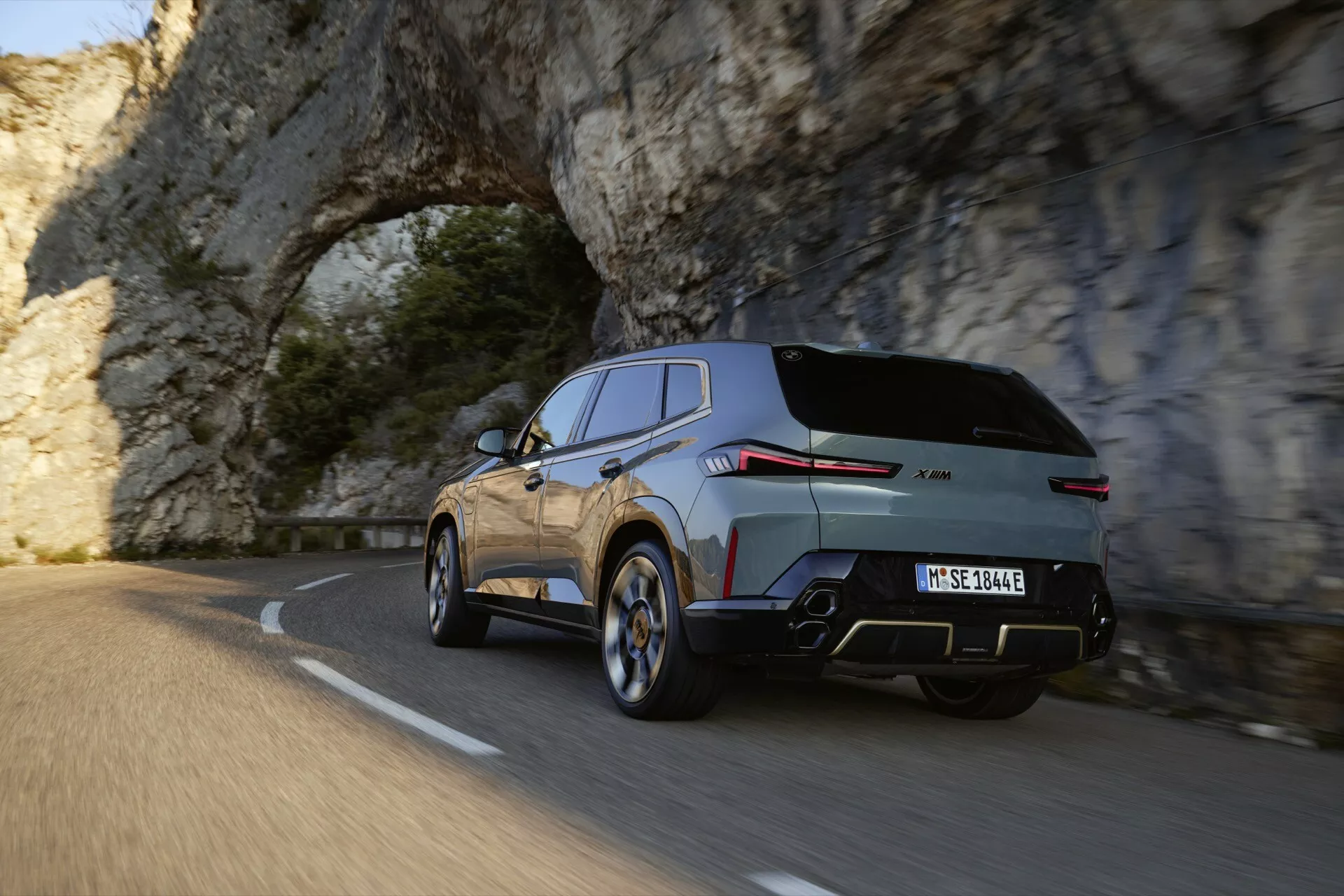 2023 BMW XM (G09) showcasing dynamic rear three-quarter view on a mountain road with sporty silhouette, metallic paint, and advanced design features