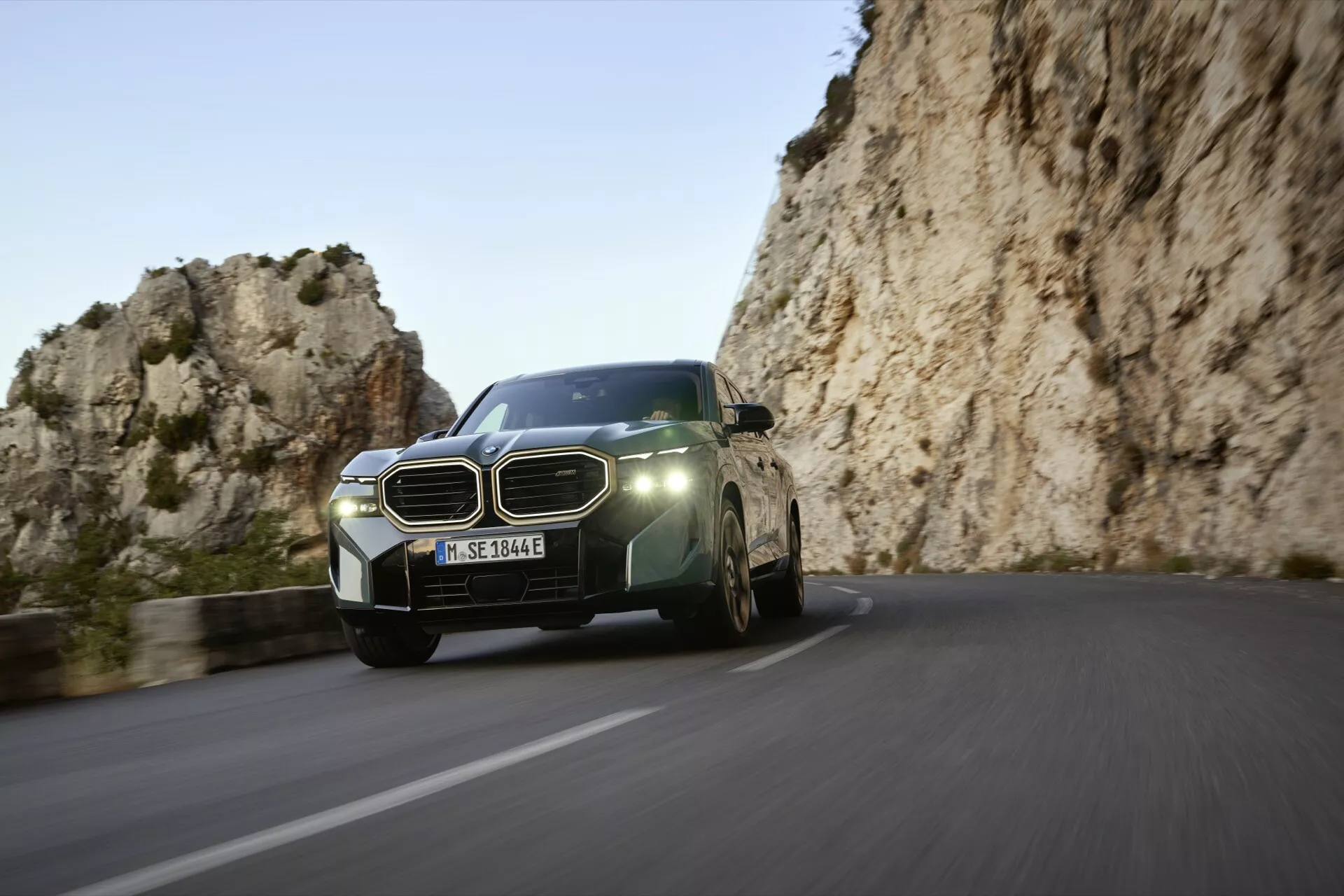 2023 BMW XM (G09) dynamic front three-quarter view on a winding mountain road, showcasing modern LED headlights, large grille, aerodynamic design, and advanced technology features.