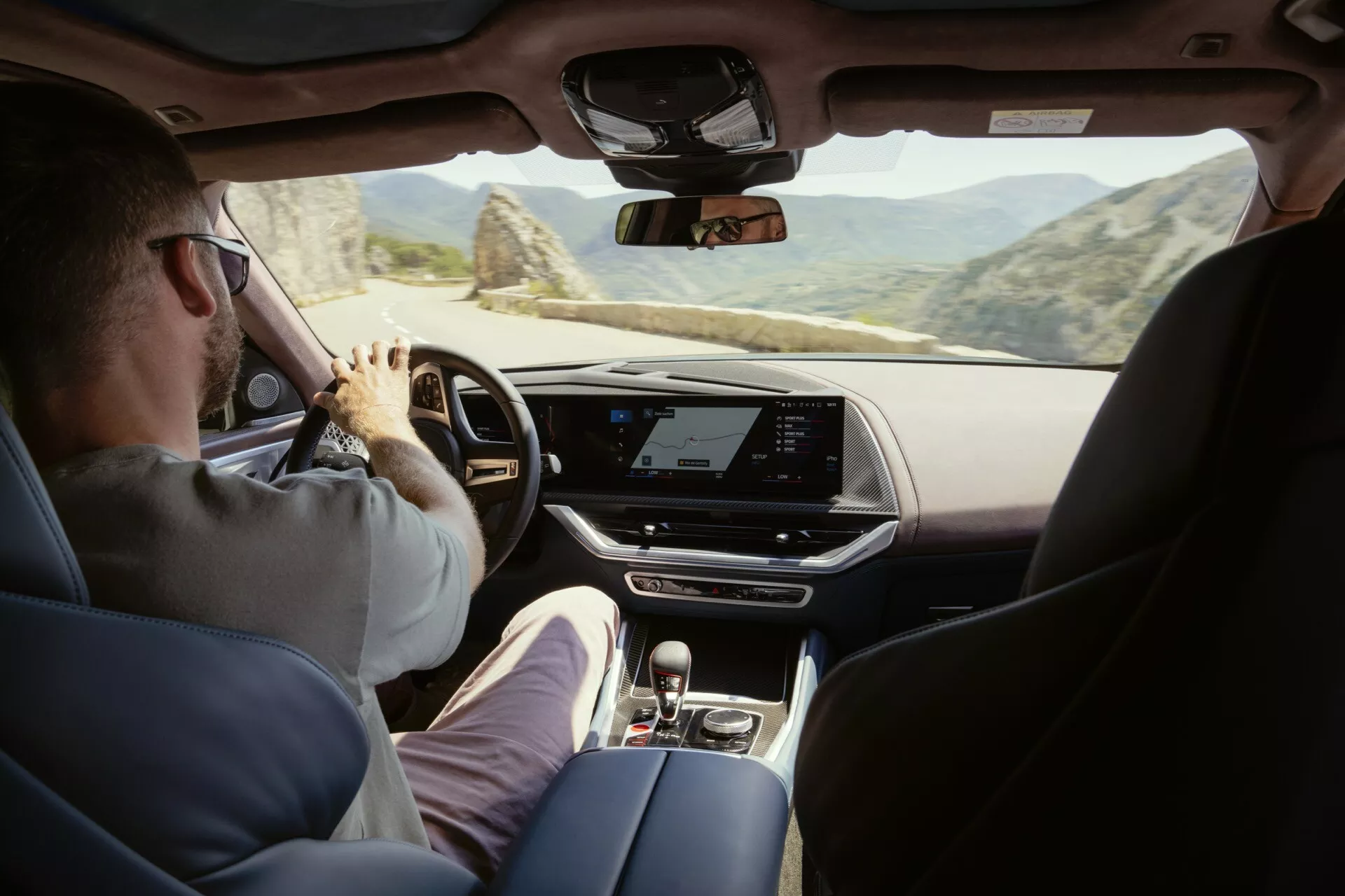 2023 BMW XM (G09) interior view from the backseat showing the dashboard, center console, touchscreen infotainment display, and partial view of driver and front passenger seats